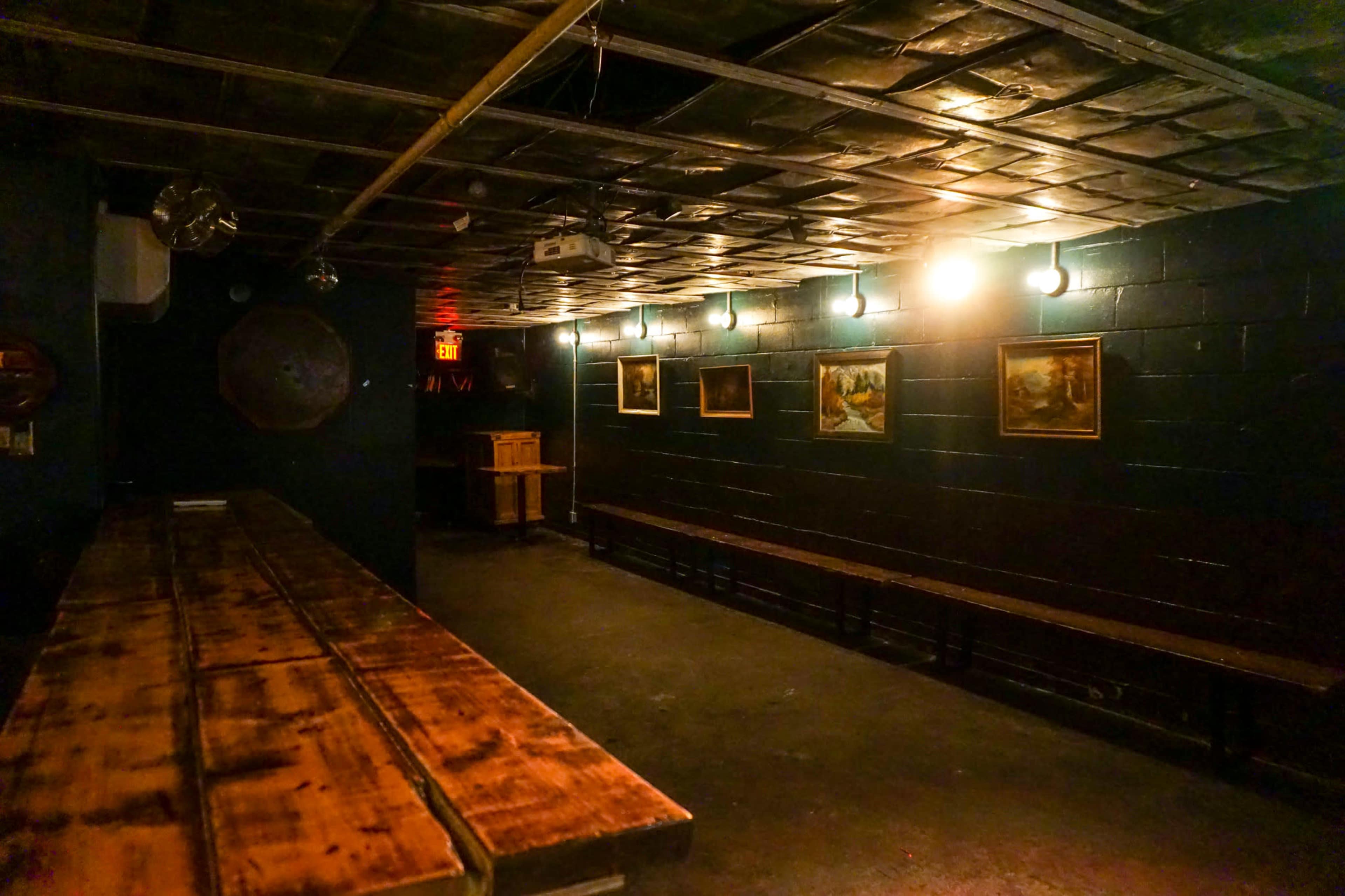 A dimly lit room with wooden benches along the walls and framed paintings hung on the dark-painted walls.