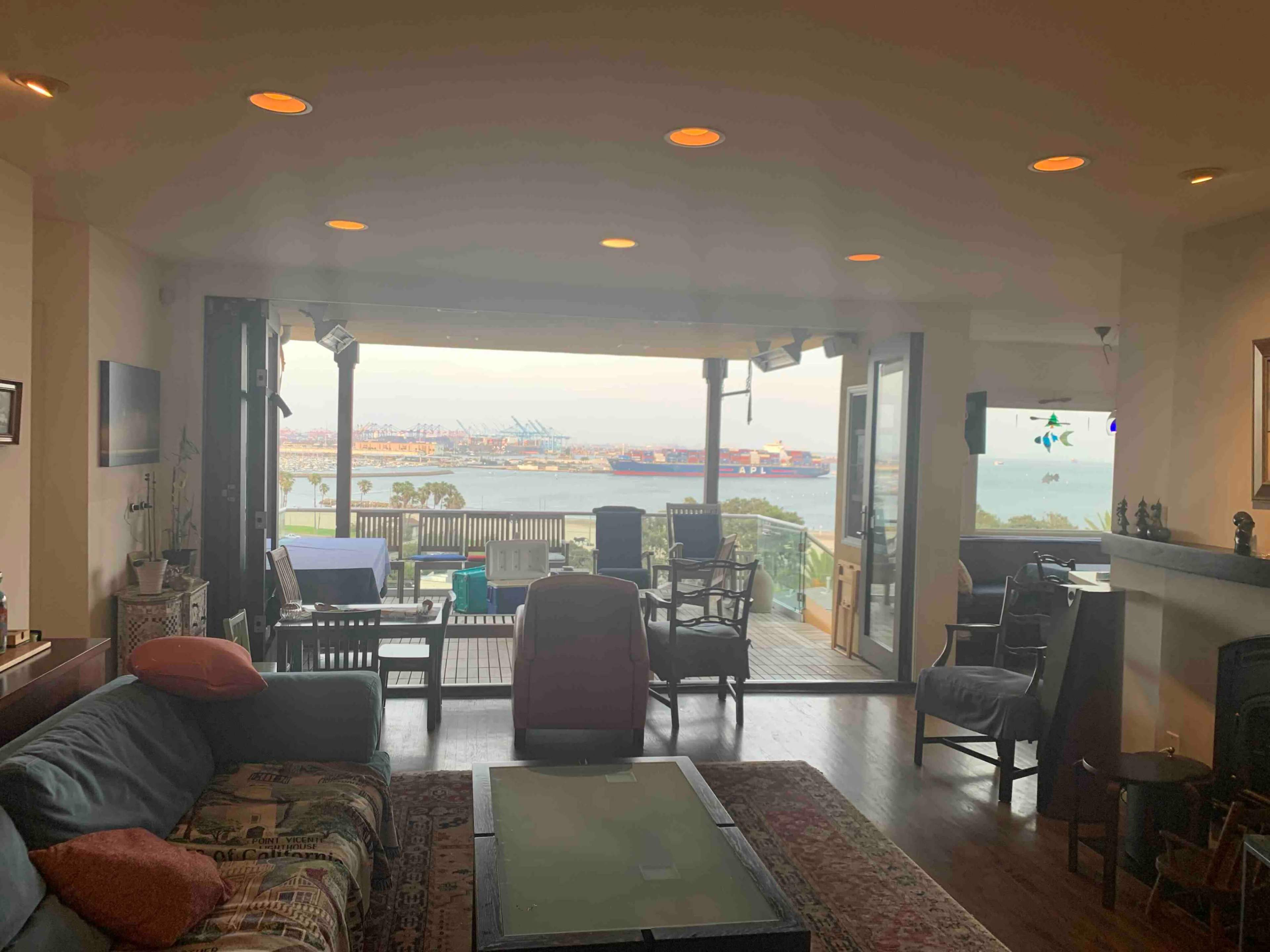 A cozy living room with large windows overlooking a harbor filled with ships.