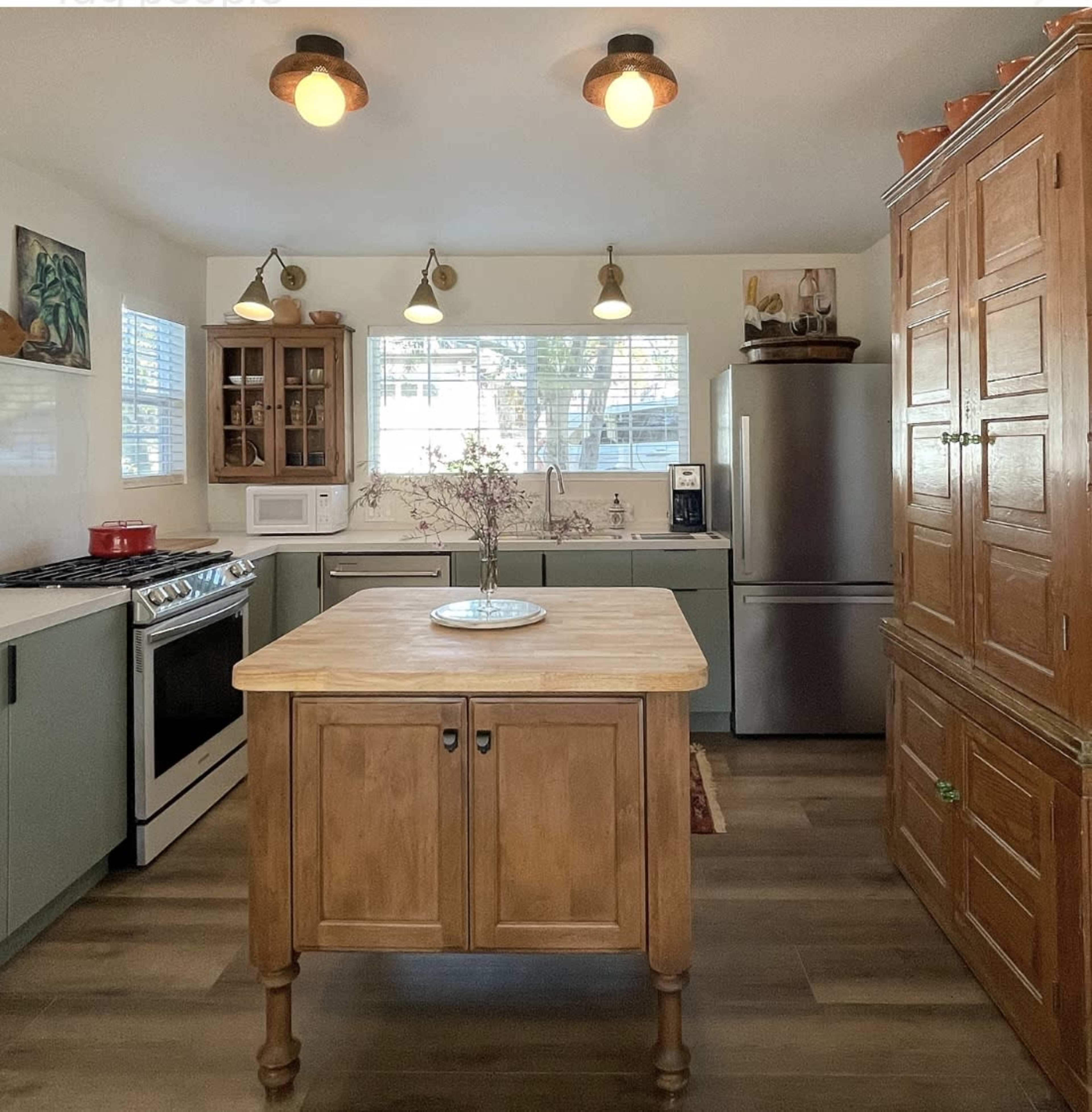 A modern kitchen features a central wooden island, a gas stove, stainless steel refrigerator, and a dining area with natural light from the windows.
