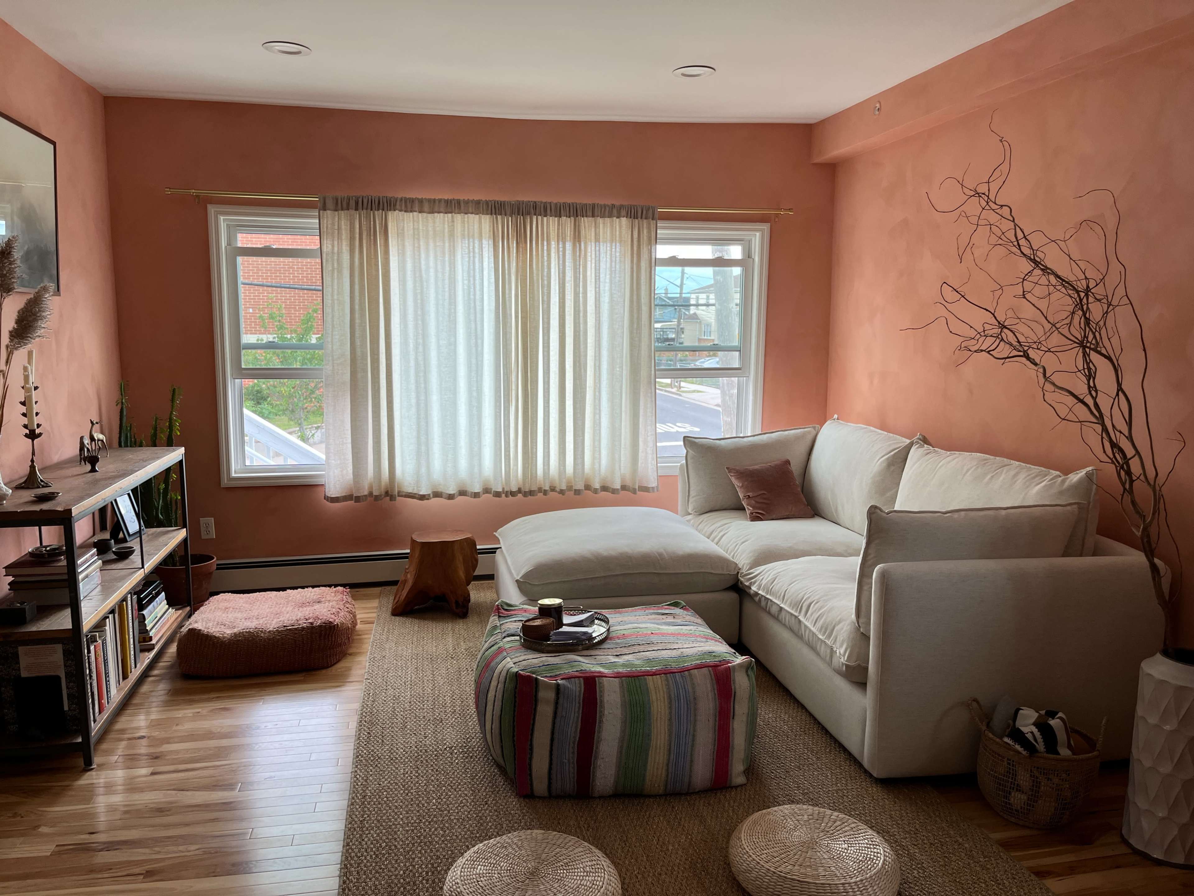 A cozy living room with a light-colored sectional sofa, a woven rug, and large windows covered by sheer curtains.
