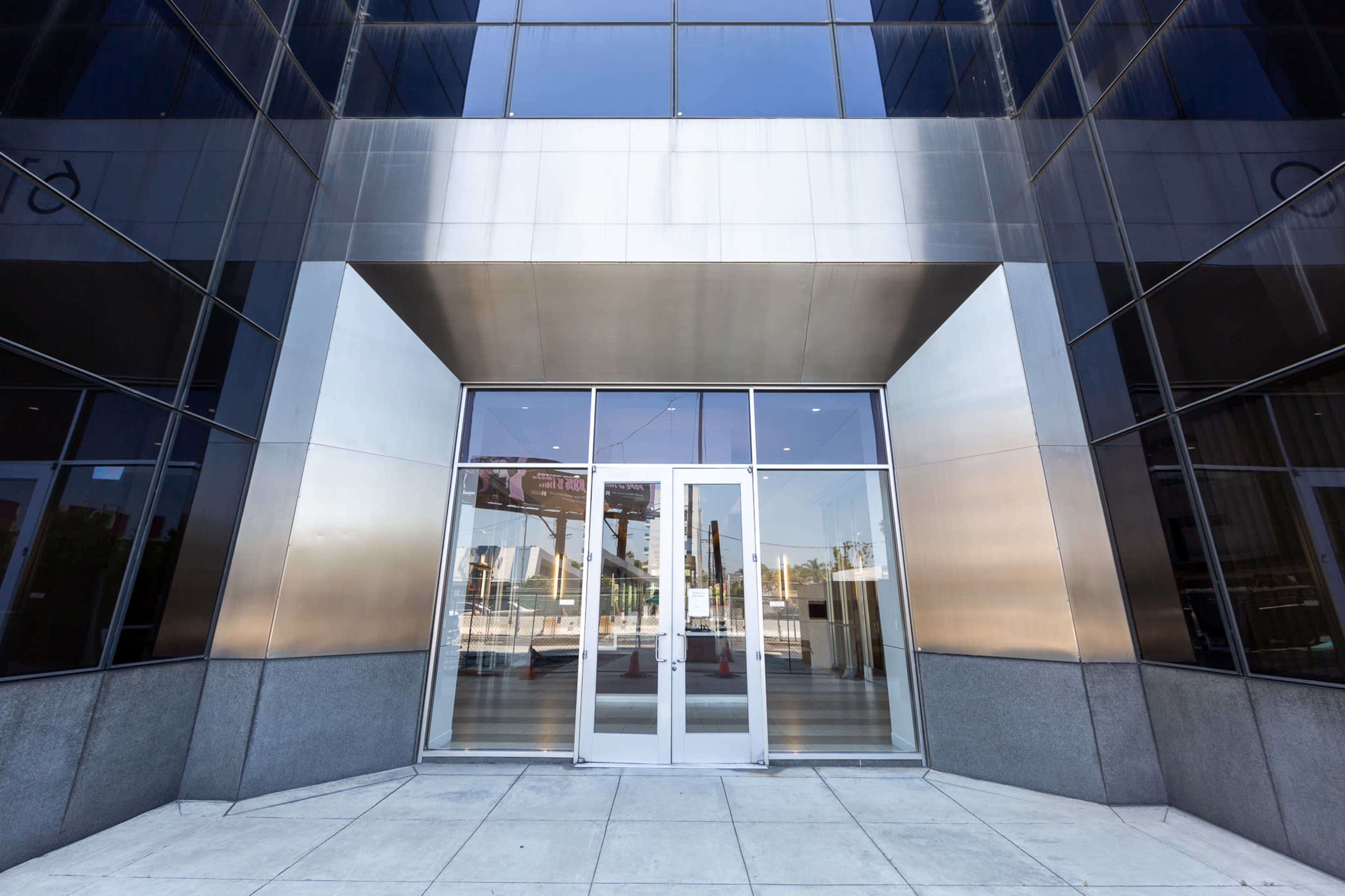 The image shows the entrance of a modern glass-faced building with double doors and concrete flooring.