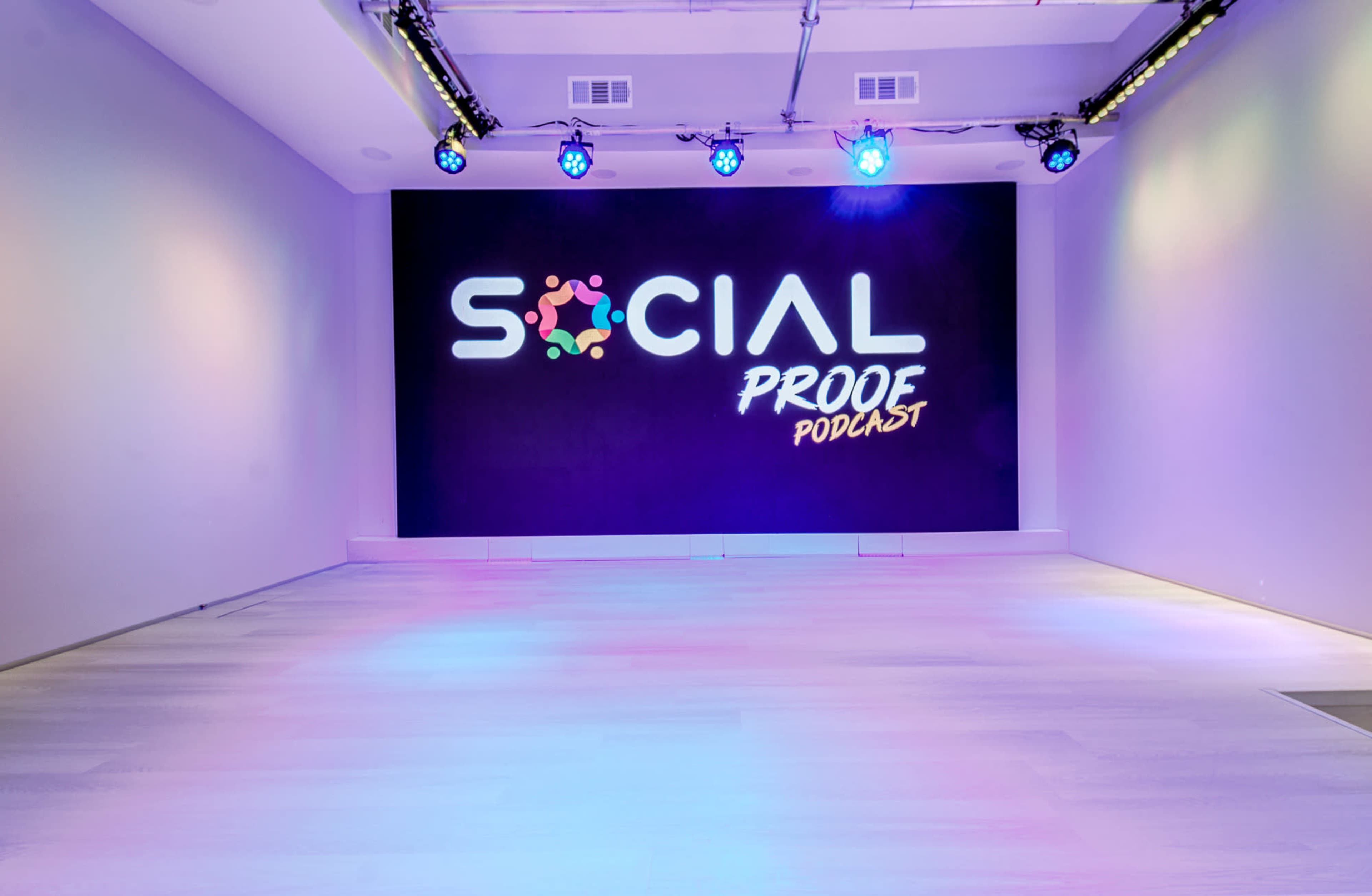 The image shows a modern studio space featuring a large screen displaying the words "SOCIAL PROOF PODCAST" with colorful lighting.