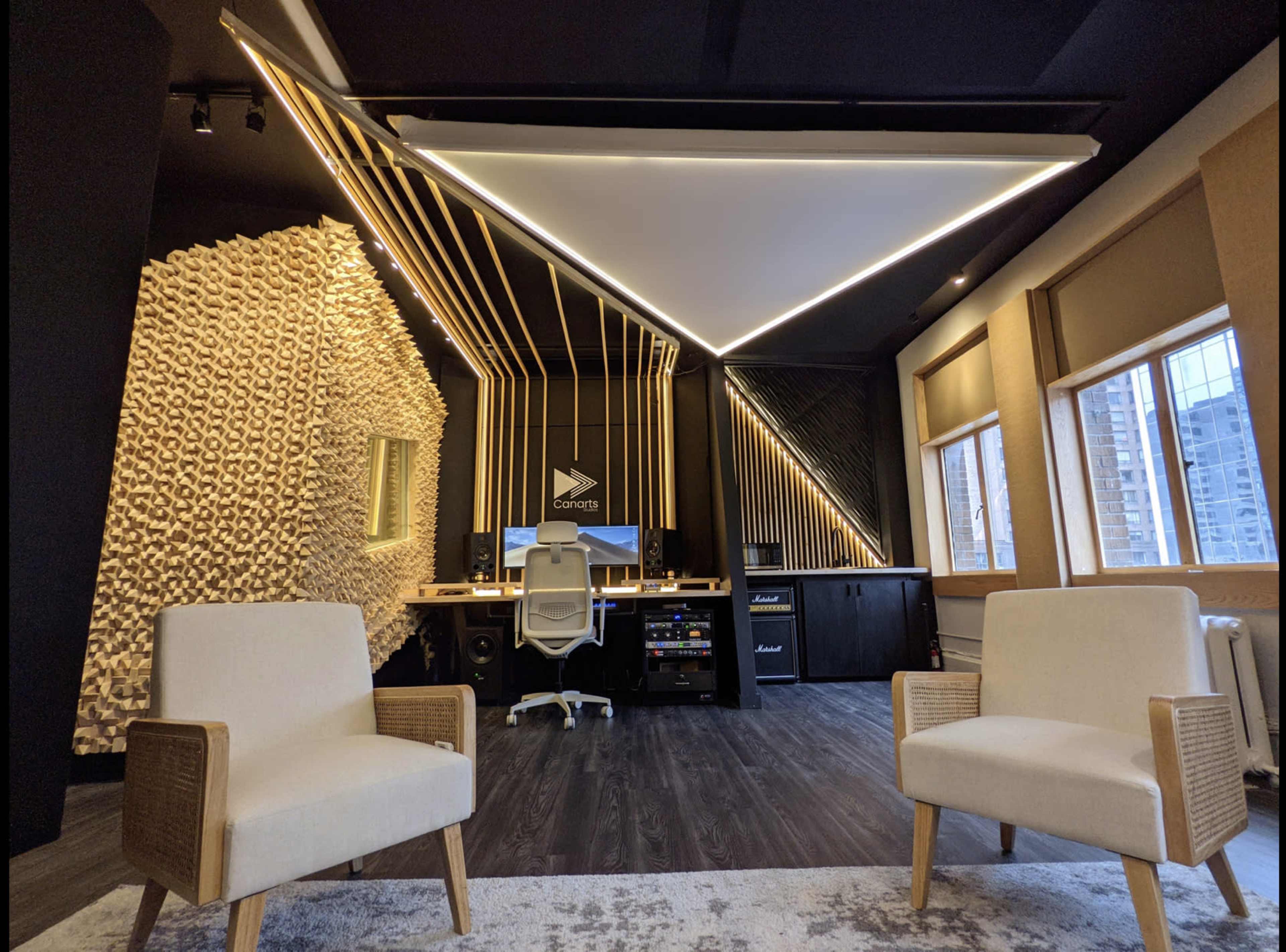A modern office space with two white chairs facing a sleek desk setup featuring a computer and musical equipment, against a backdrop of geometric wall designs.