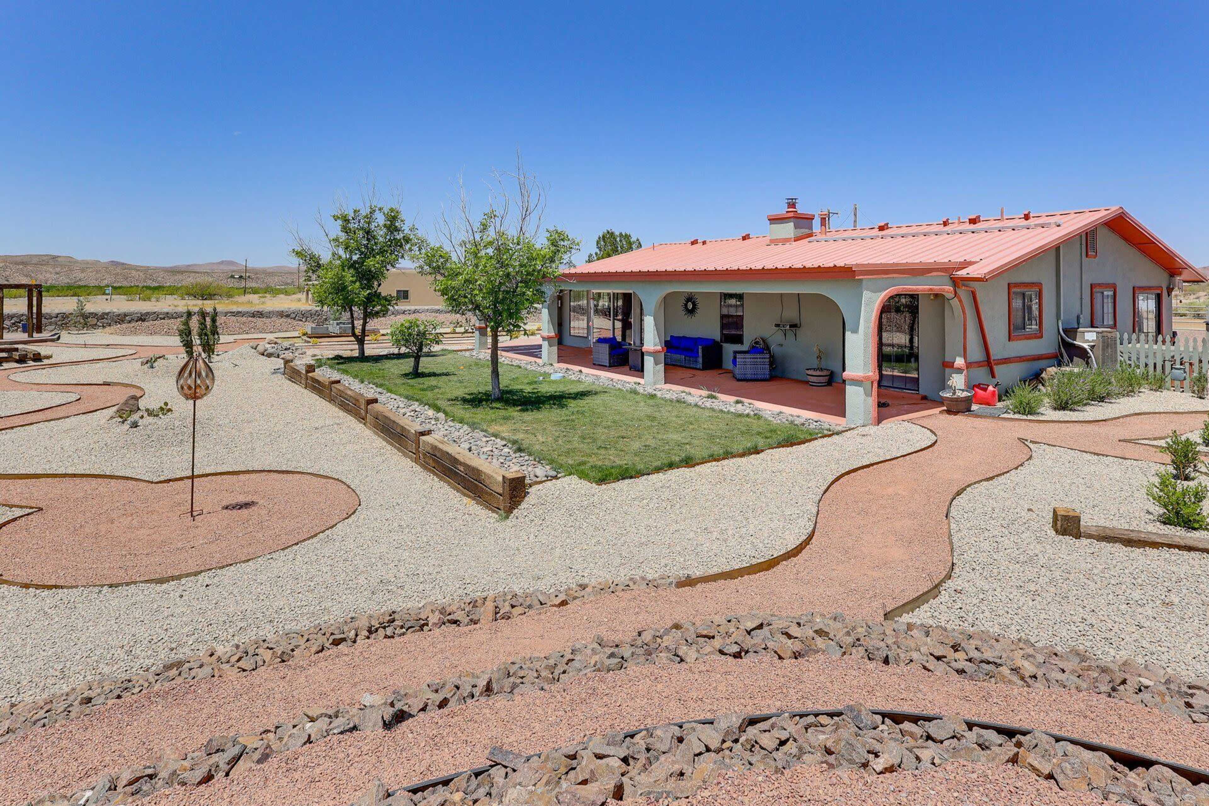 A red-roofed house with a landscaped yard featuring gravel paths and decorative rocks is set against a clear blue sky.