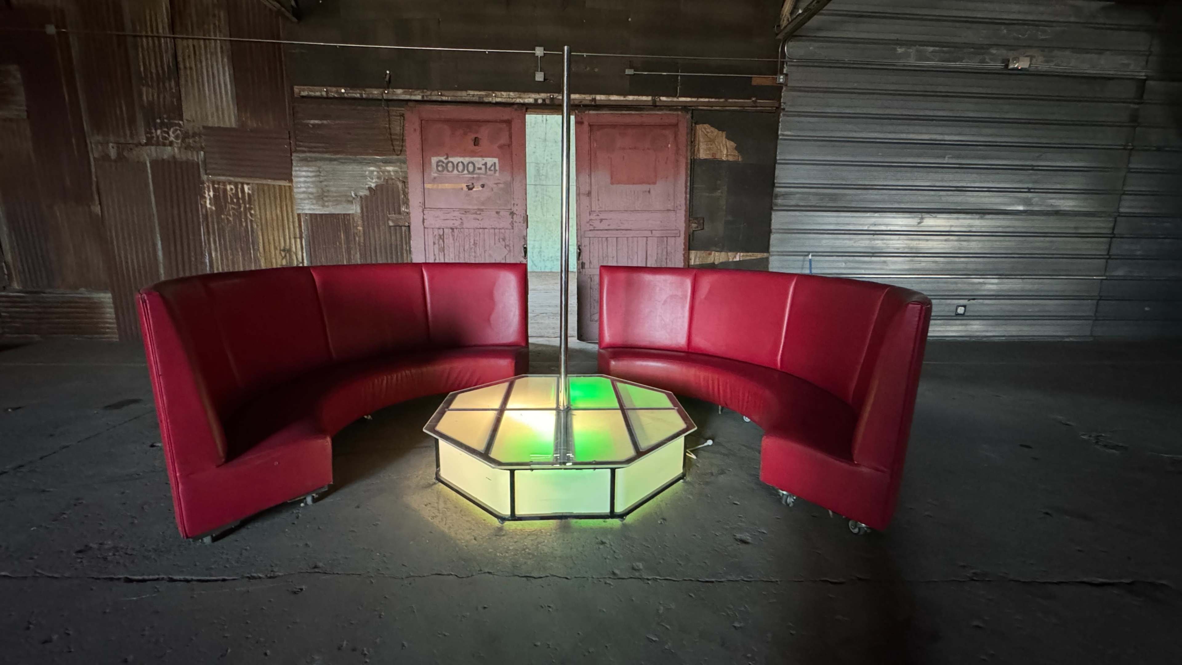 The image shows a seating area with two curved red benches arranged around a hexagonal table featuring a central pole and colored lights.