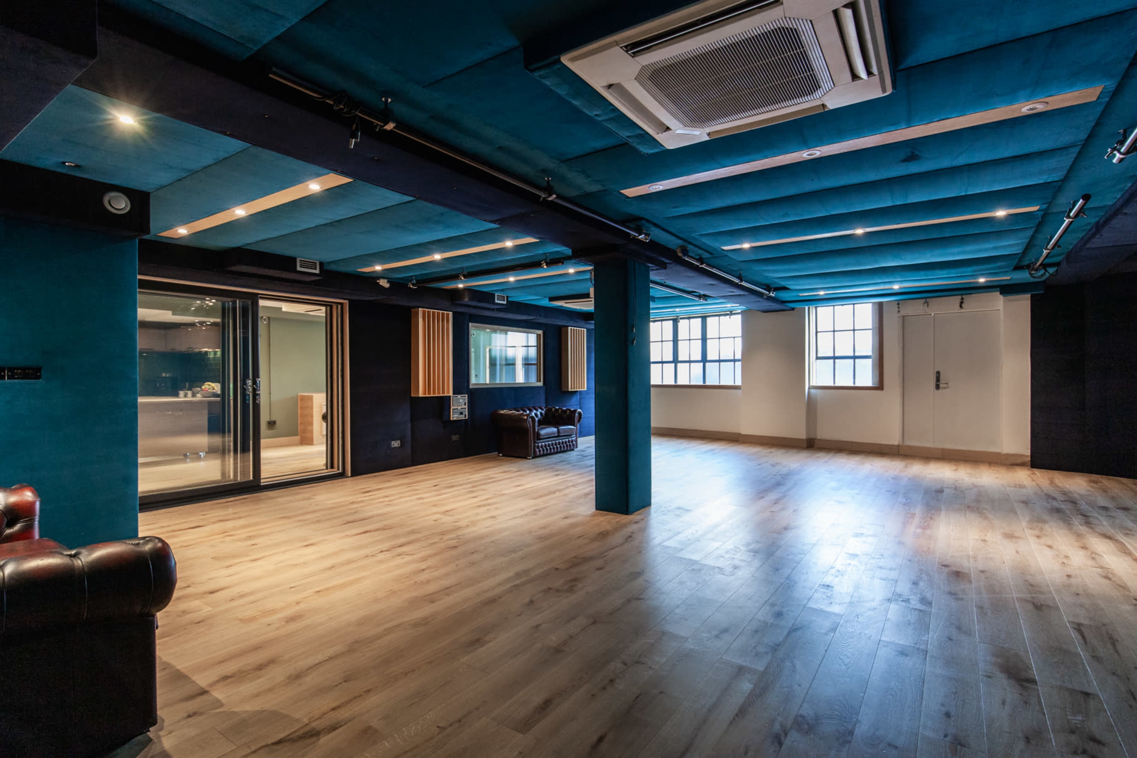 A spacious room with blue acoustic panels, wooden flooring, and large glass doors leading to another area.