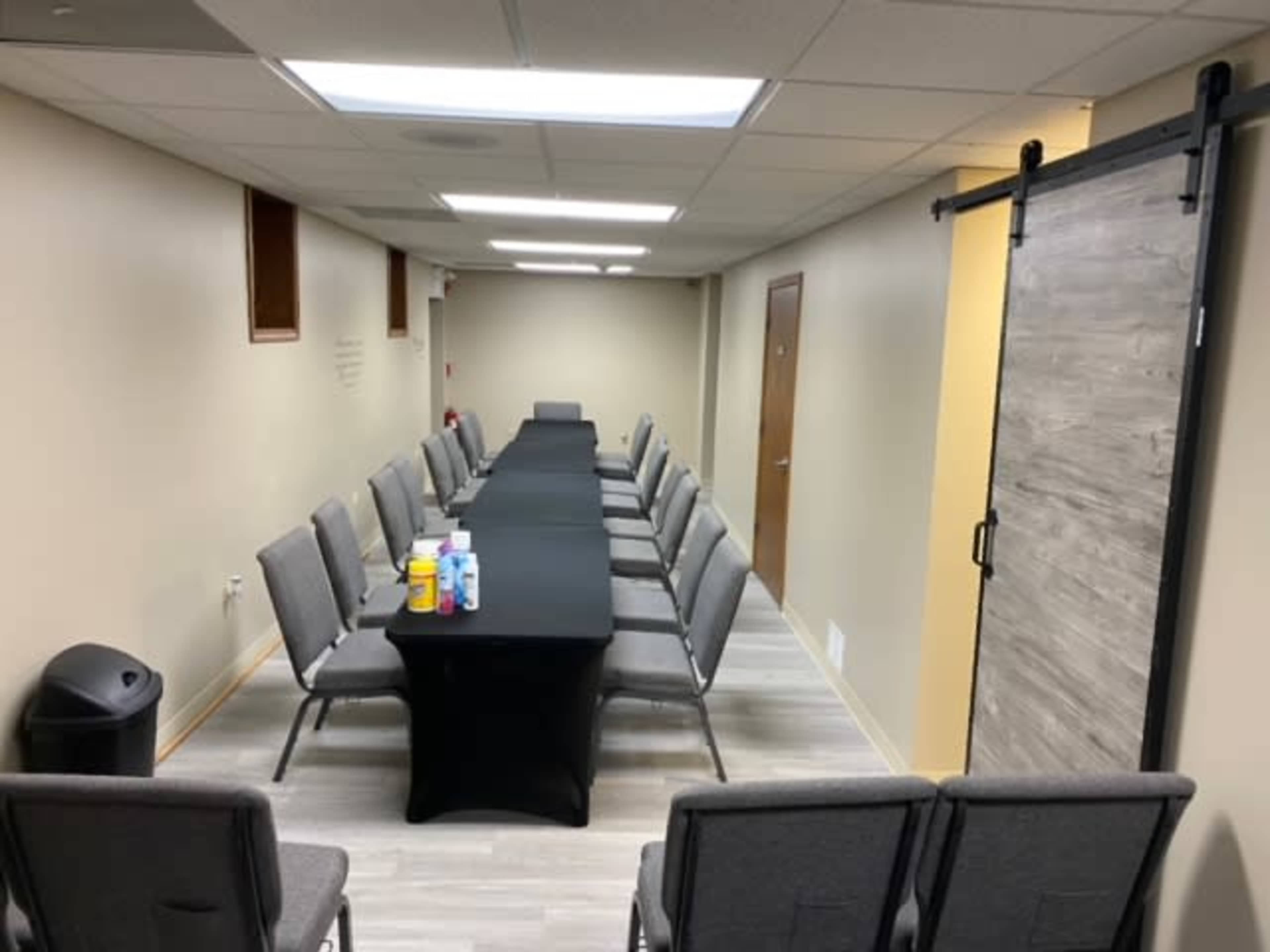 A long table covered with a black tablecloth is set in a narrow meeting room with chairs arranged on either side.