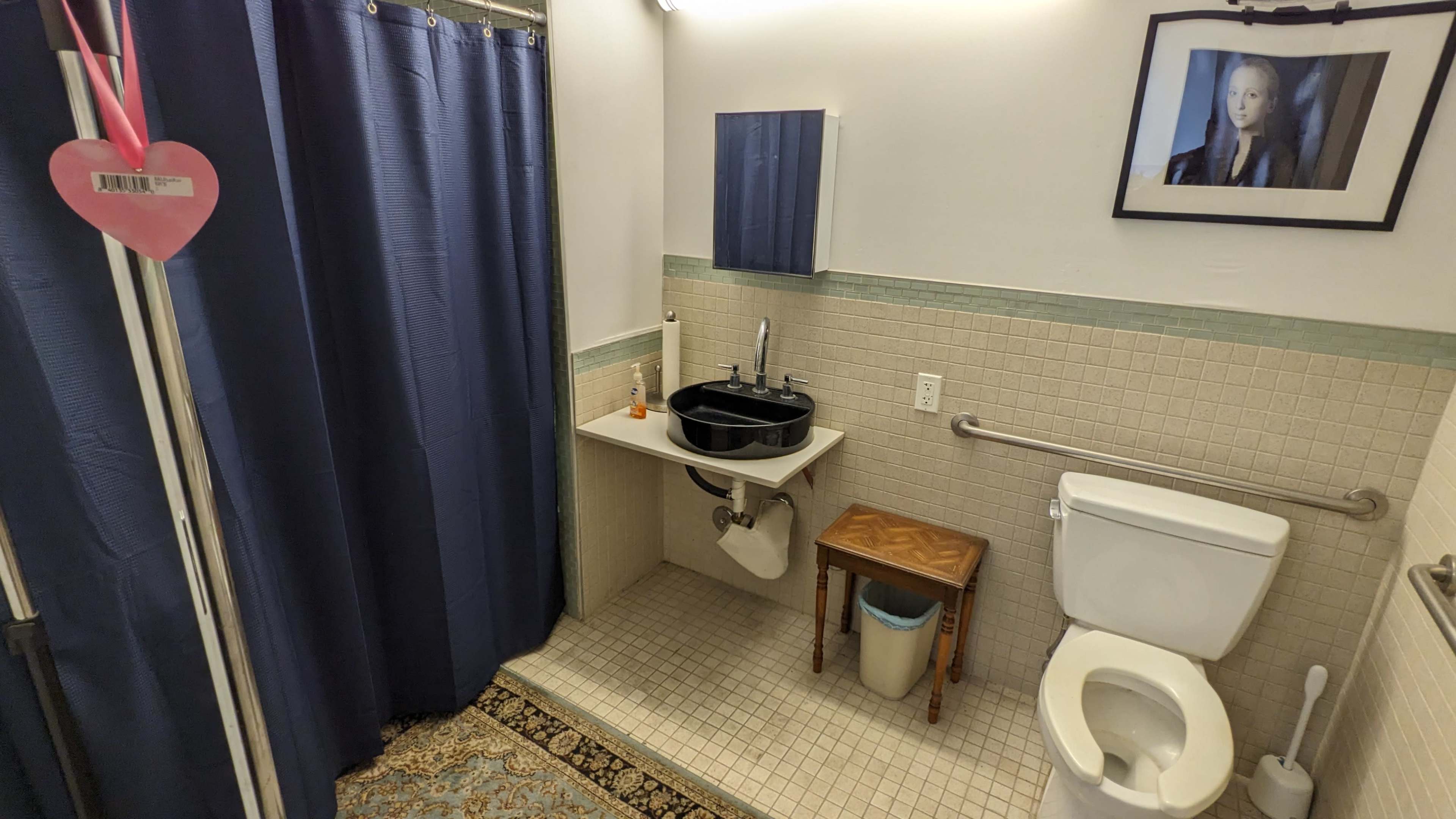 The image shows a small bathroom with a toilet, a sink with a black basin, and a shower area, all featuring navy blue curtains and beige tiled walls.