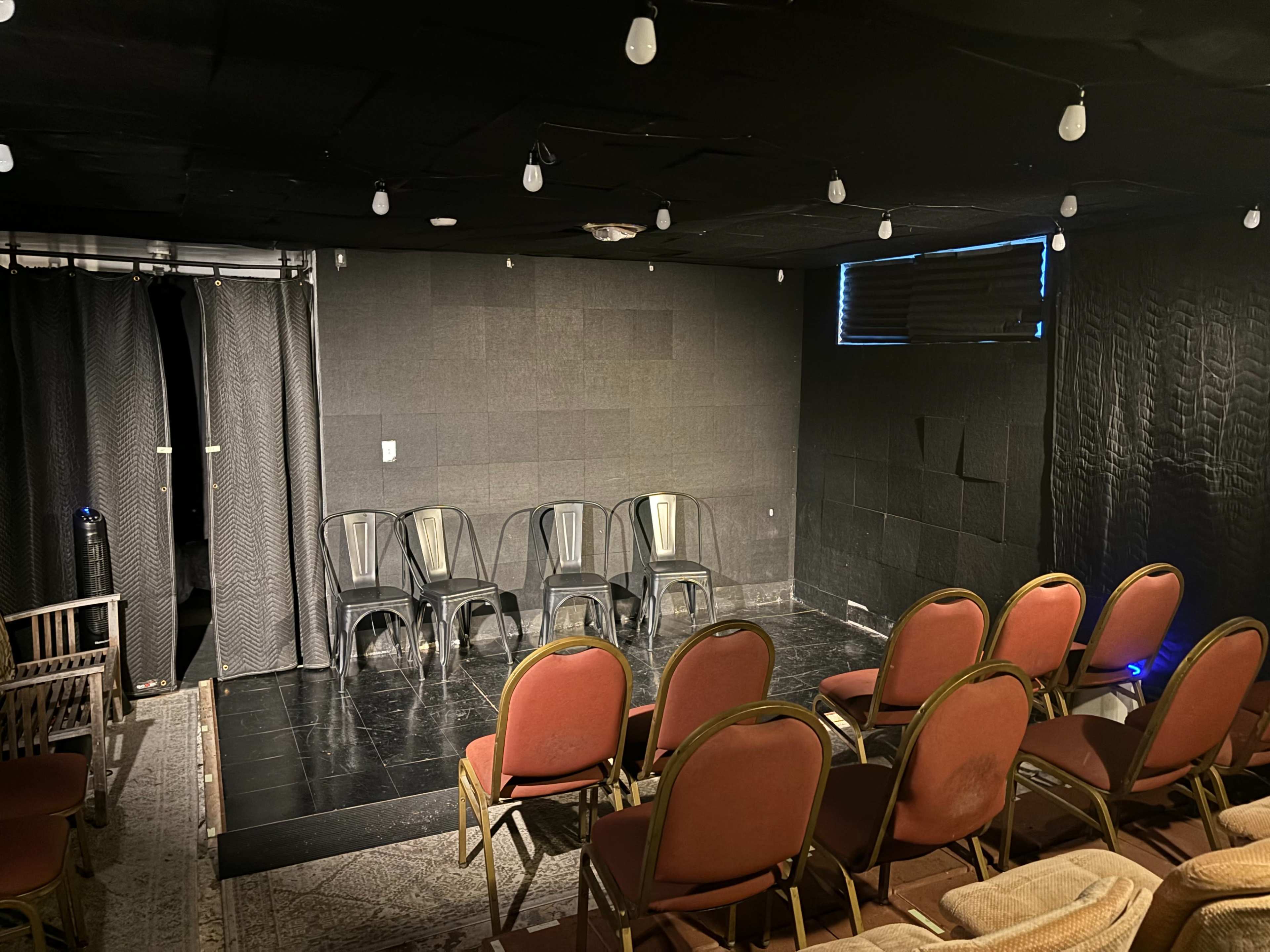 A small theater with black walls, a stage area, and rows of red chairs arranged for an audience.