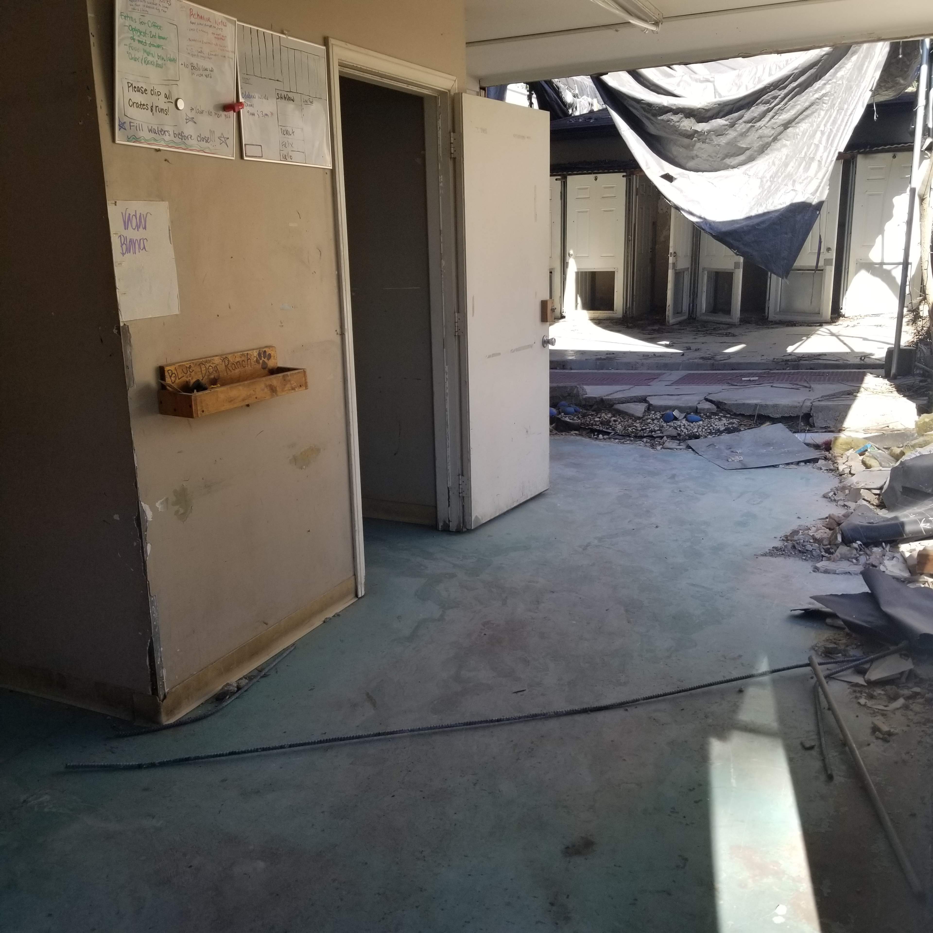 An empty, partially renovated indoor space with open doors leading to other rooms and debris scattered on the floor.