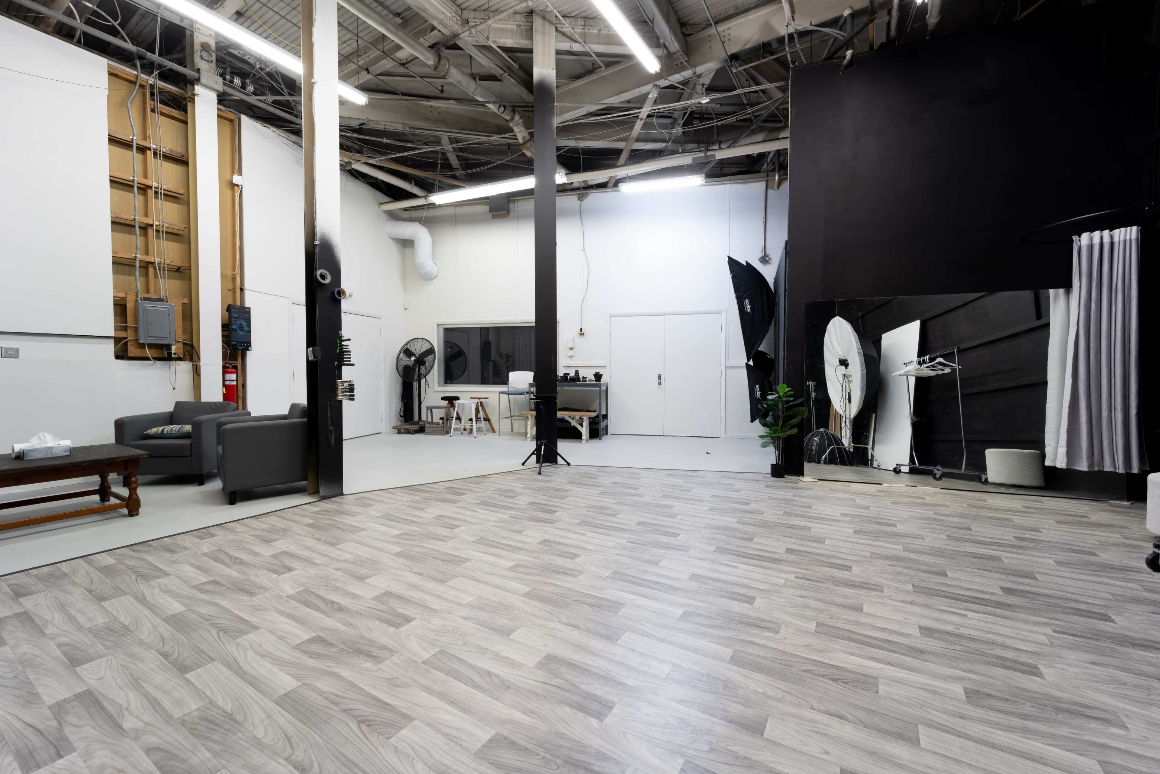An empty studio space with a wooden floor, large black and white backdrops, and various studio equipment set up.