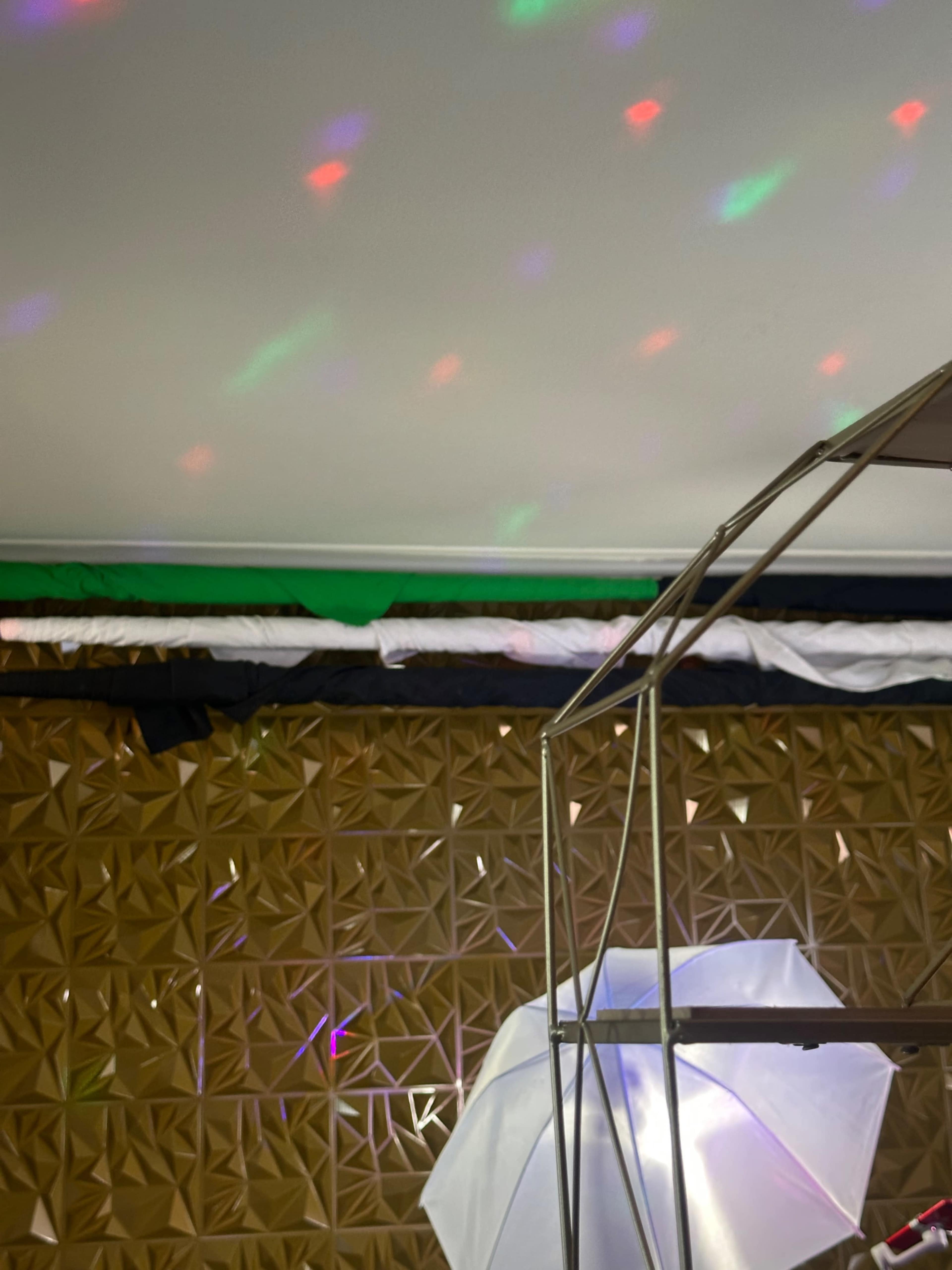 The image shows a ceiling with colorful light reflections and a partially assembled metallic frame in front of a textured brown wall.