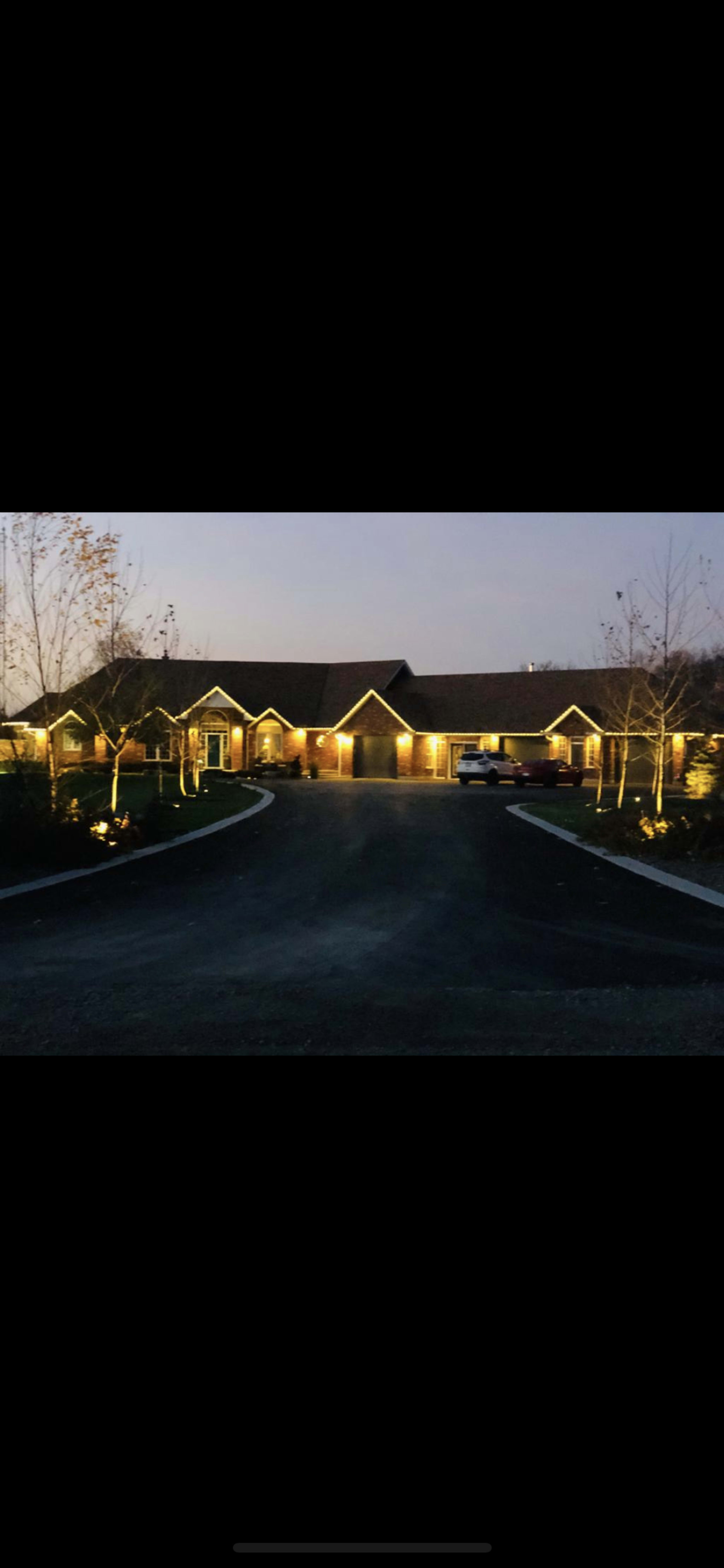 A well-lit residential building with a circular driveway, surrounded by trees at dusk.