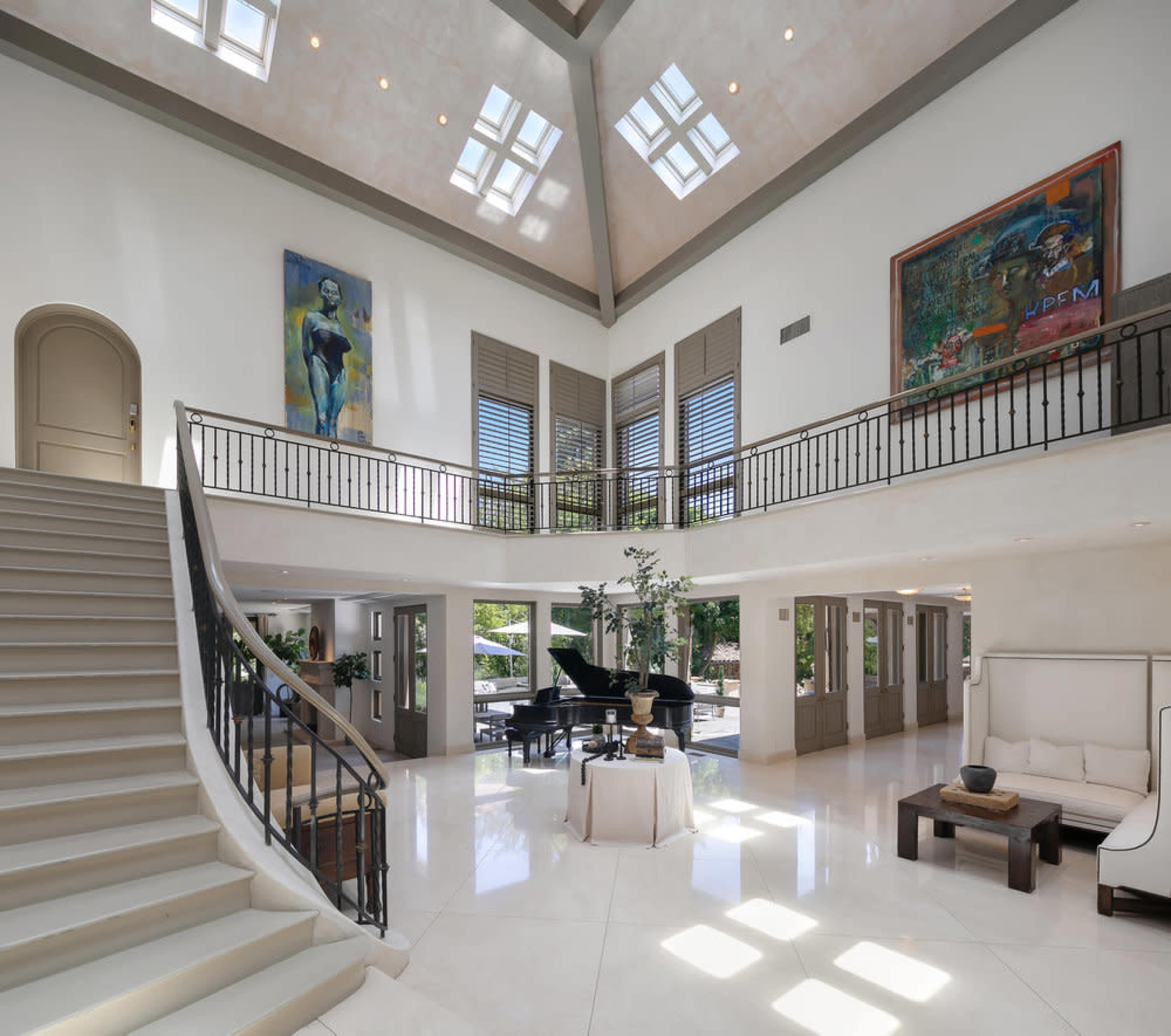 The image shows a spacious foyer with a large staircase leading to an upper level, featuring high ceilings and modern artwork on the walls.