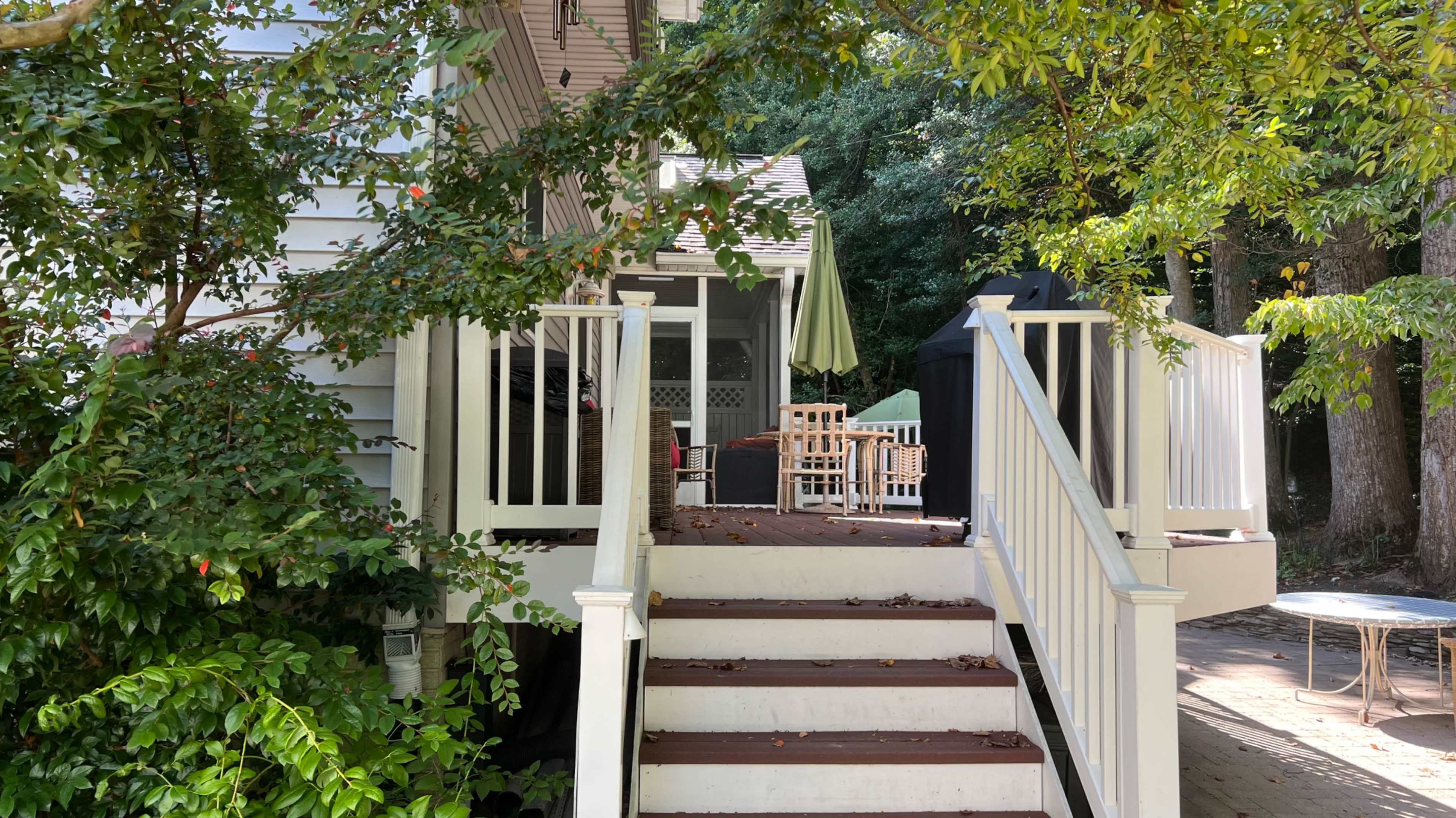 A staircase leads up to a deck with outdoor furniture, surrounded by greenery and trees.