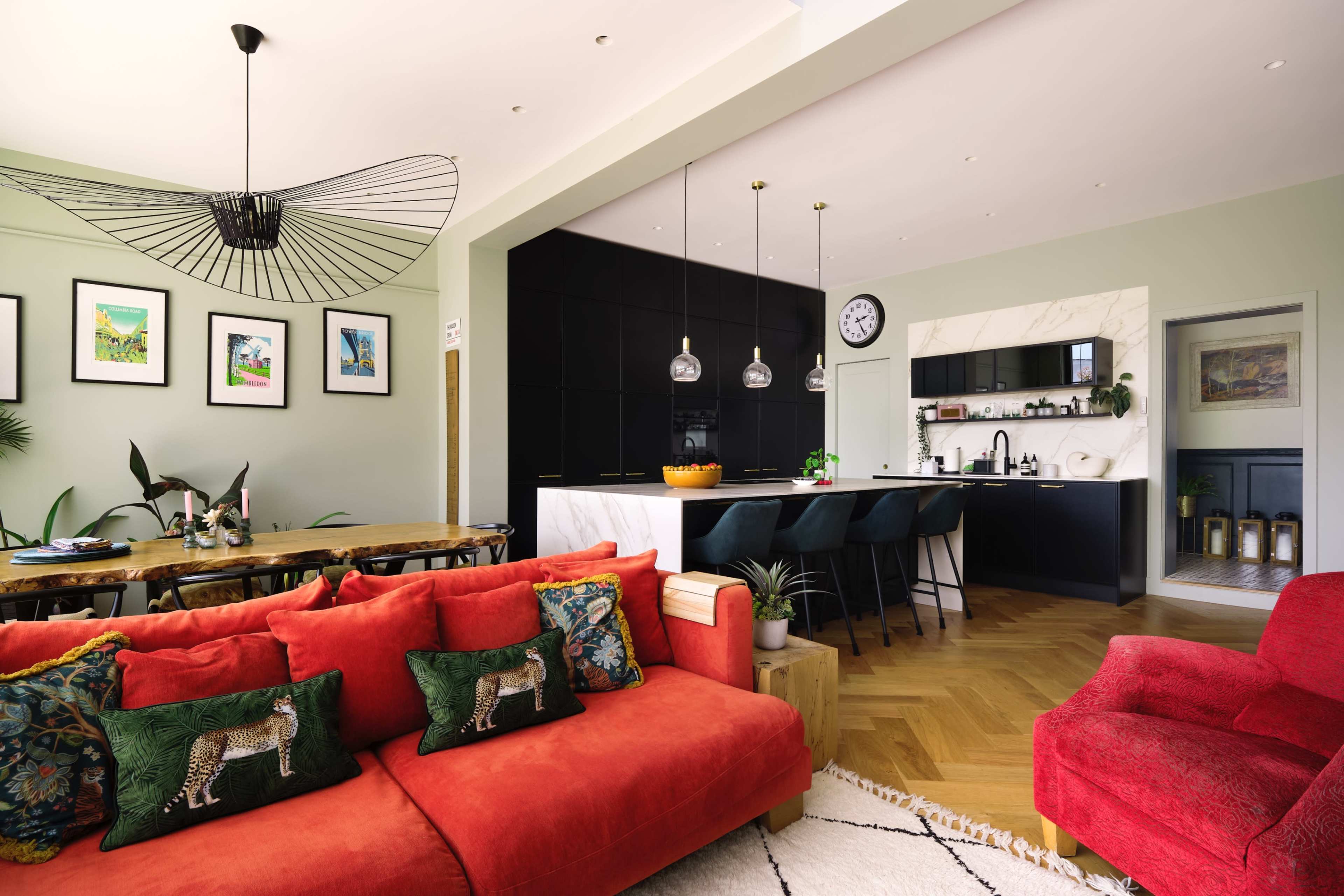 A spacious interior features a red sofa with decorative cushions, a dining table, and a kitchen with a marble island and modern appliances.