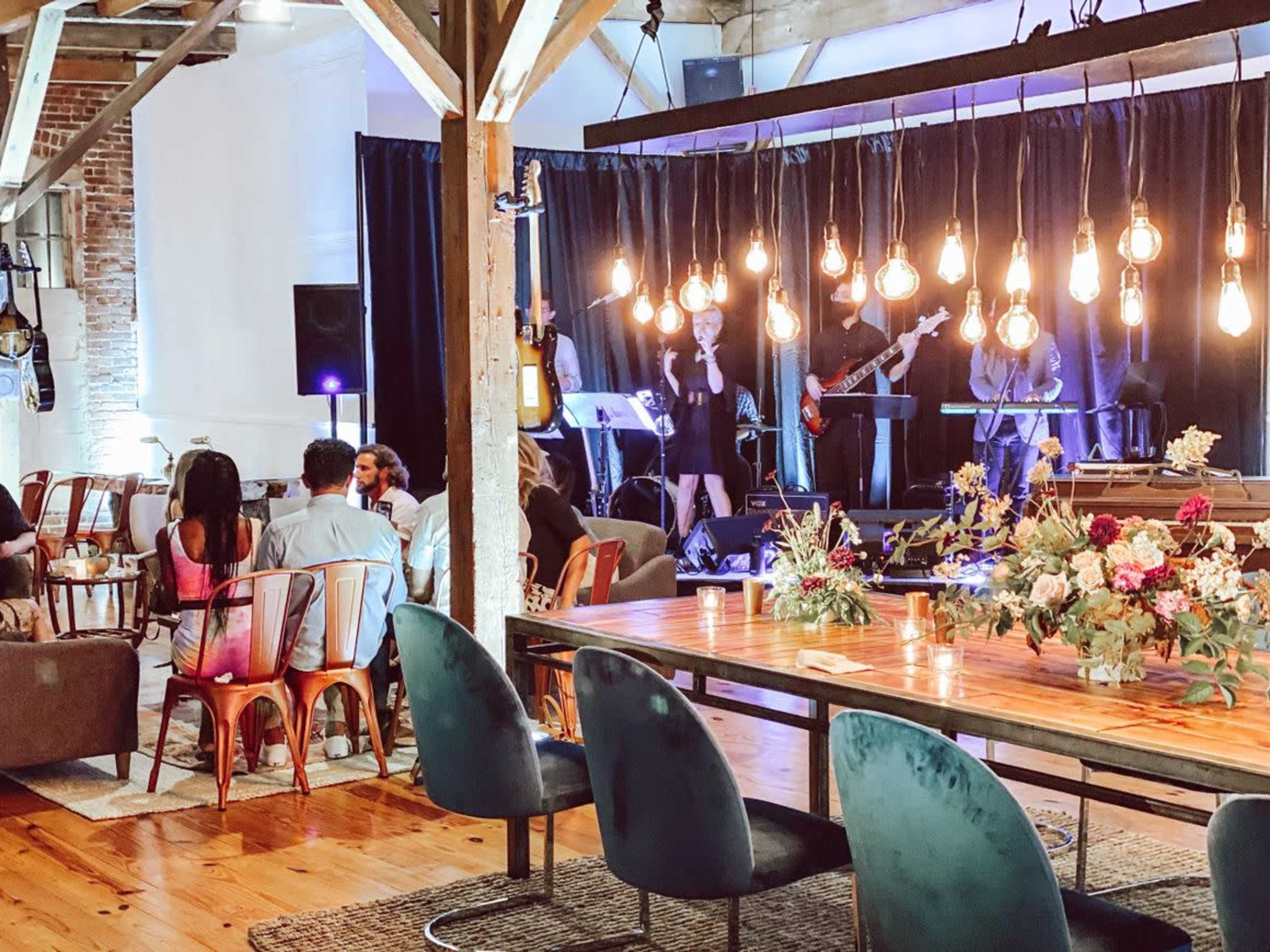 A lively indoor venue with a band performing on stage, surrounded by tables and guests socializing.