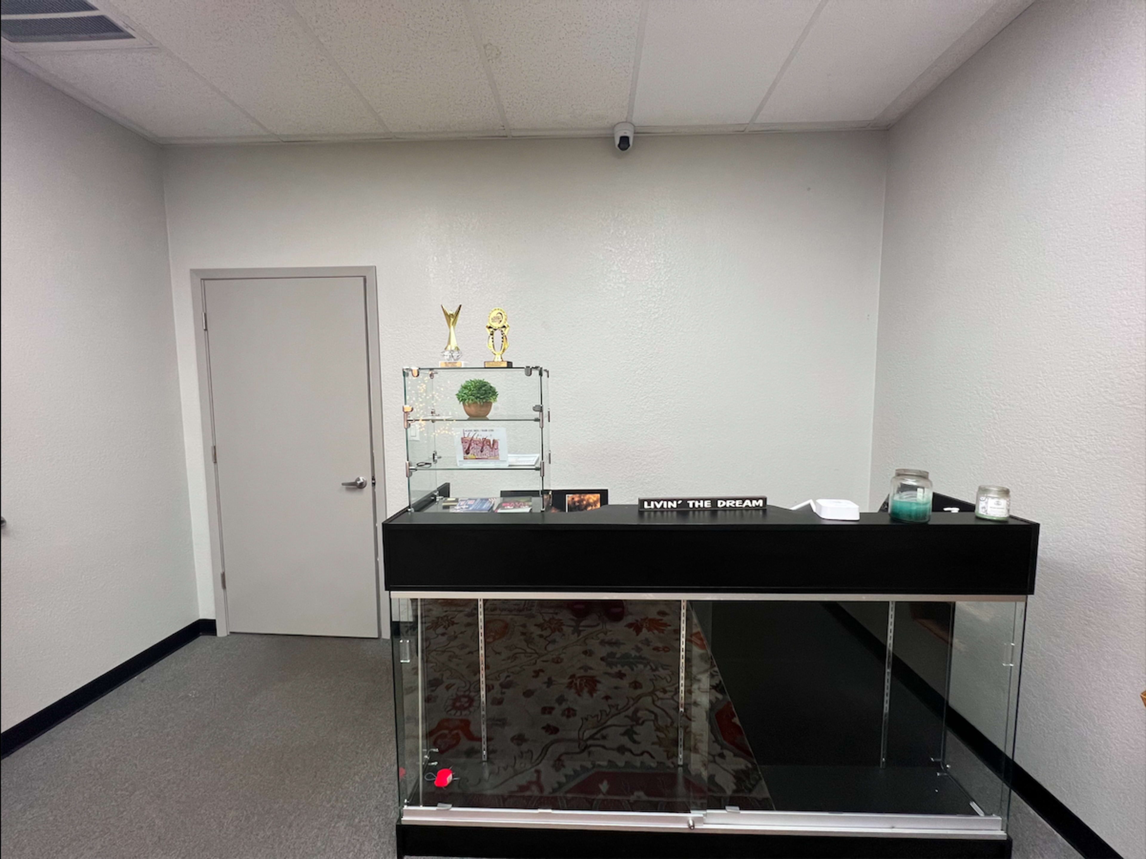 The image shows a small reception area with a glass display case and a wall-mounted camera.