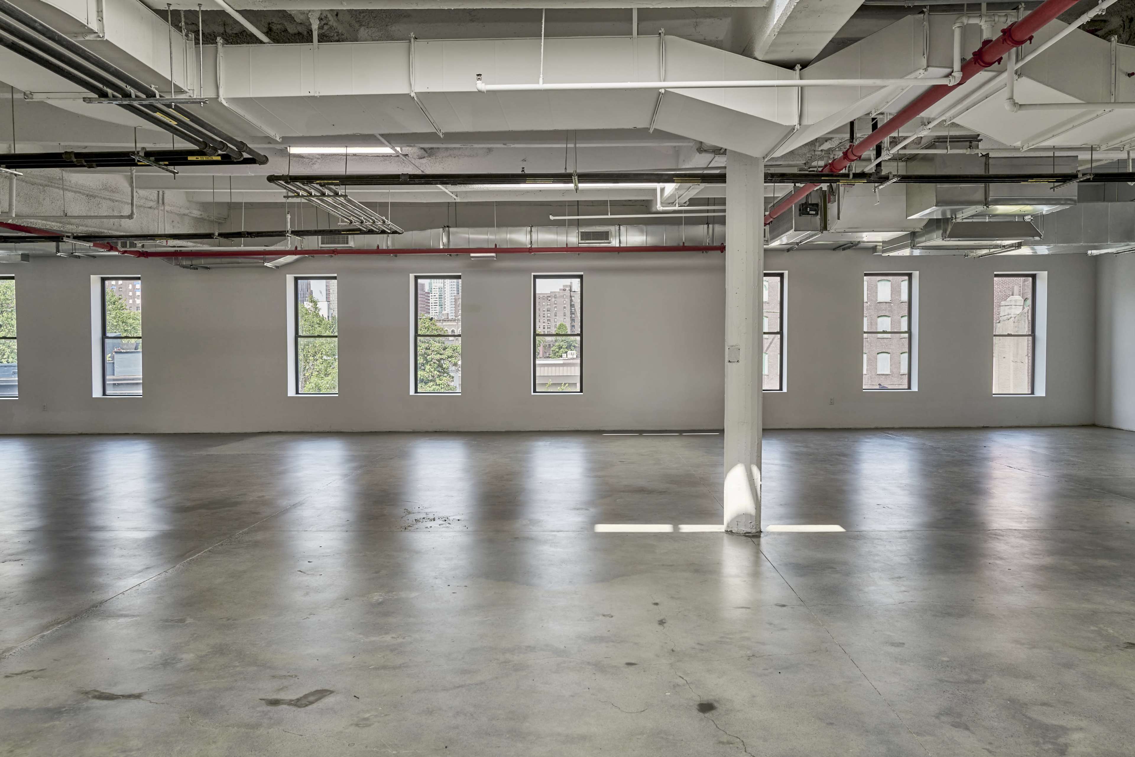 The image depicts an empty interior space with concrete flooring and several large windows along the walls.