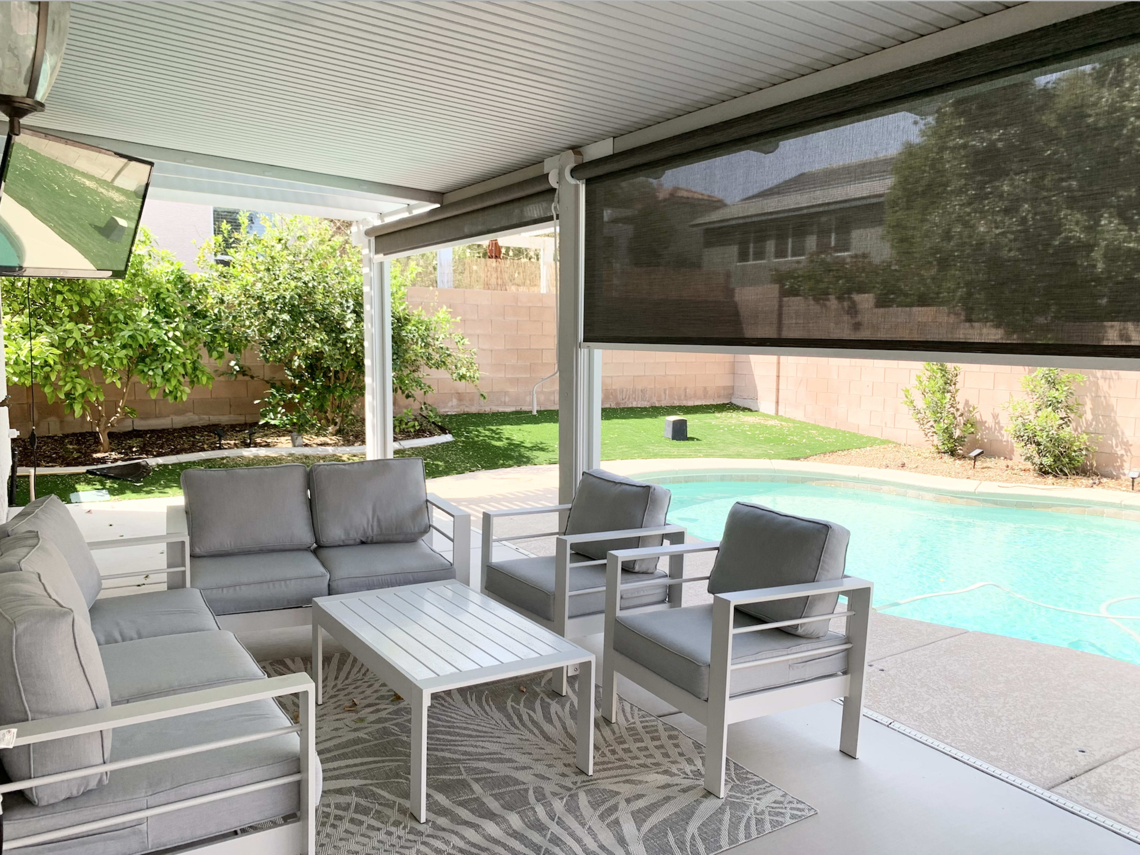 The image showcases a covered patio area with outdoor furniture overlooking a pool and landscaped yard.