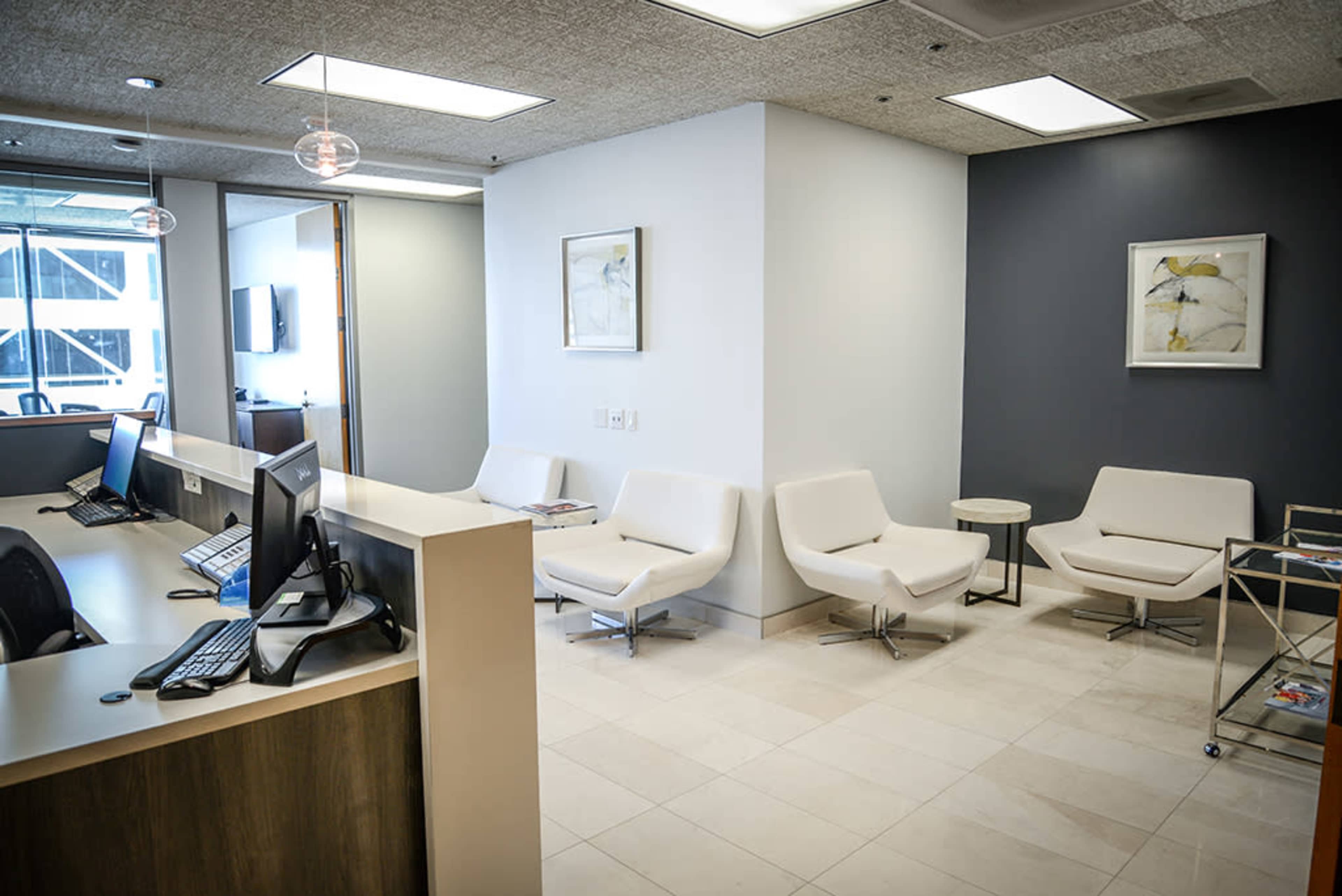 A modern waiting area with white chairs, a reception desk, and framed artwork on the walls.