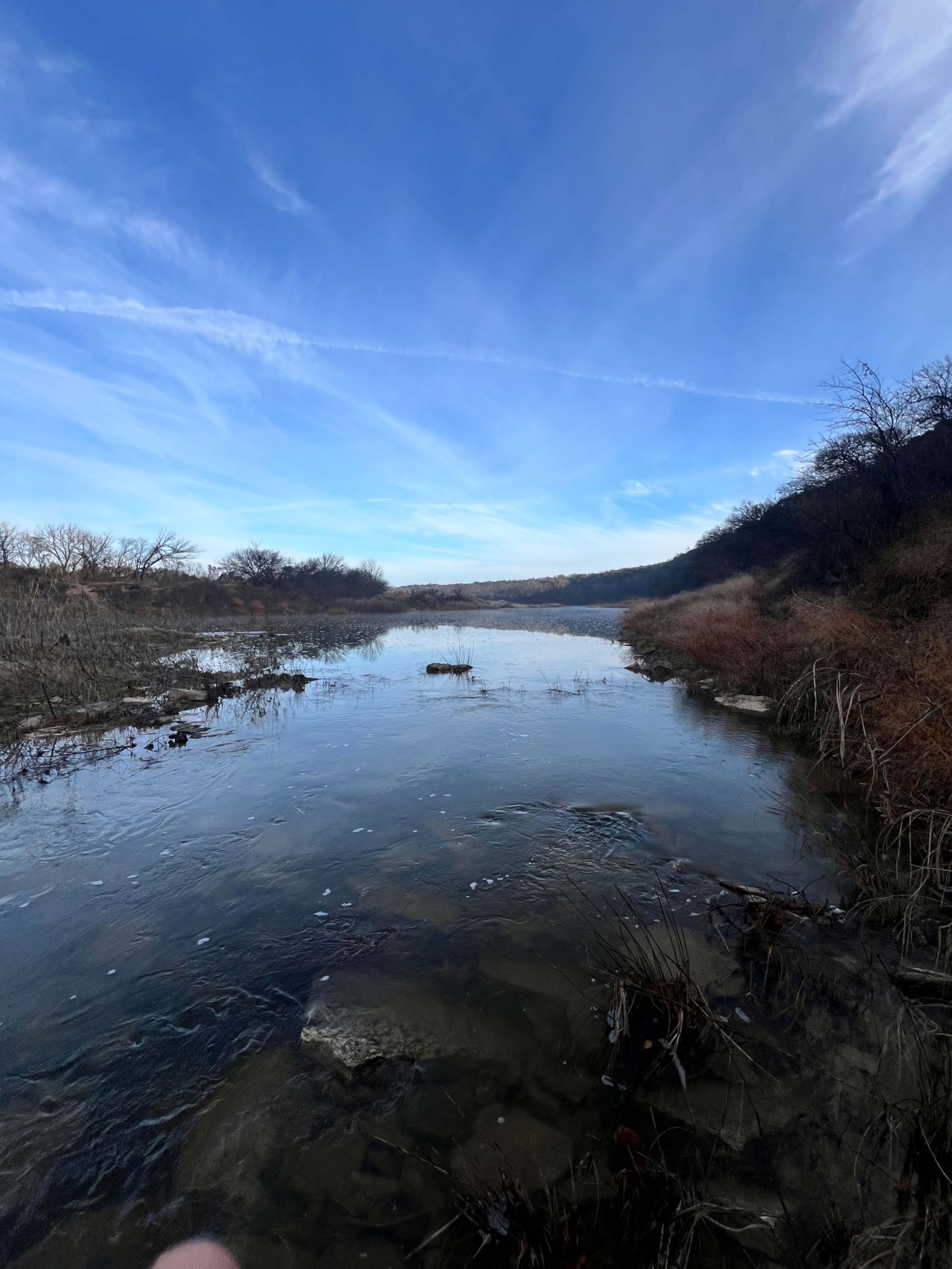 The scene shows a calm river winding through a barren landscape under a bright blue sky.
