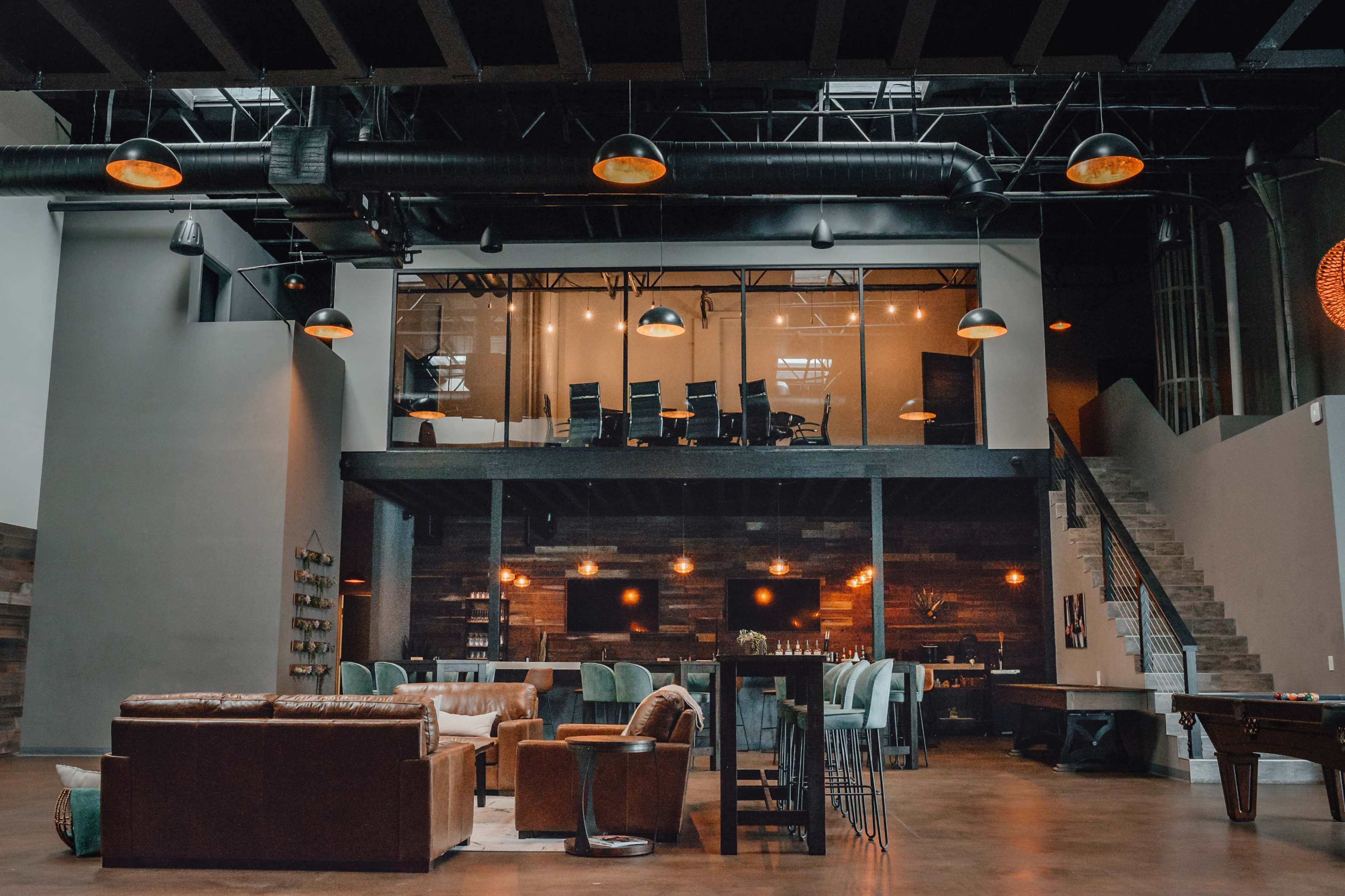 A modern, open-concept lounge area with a seating arrangement on the lower level and a glass-enclosed meeting space above.