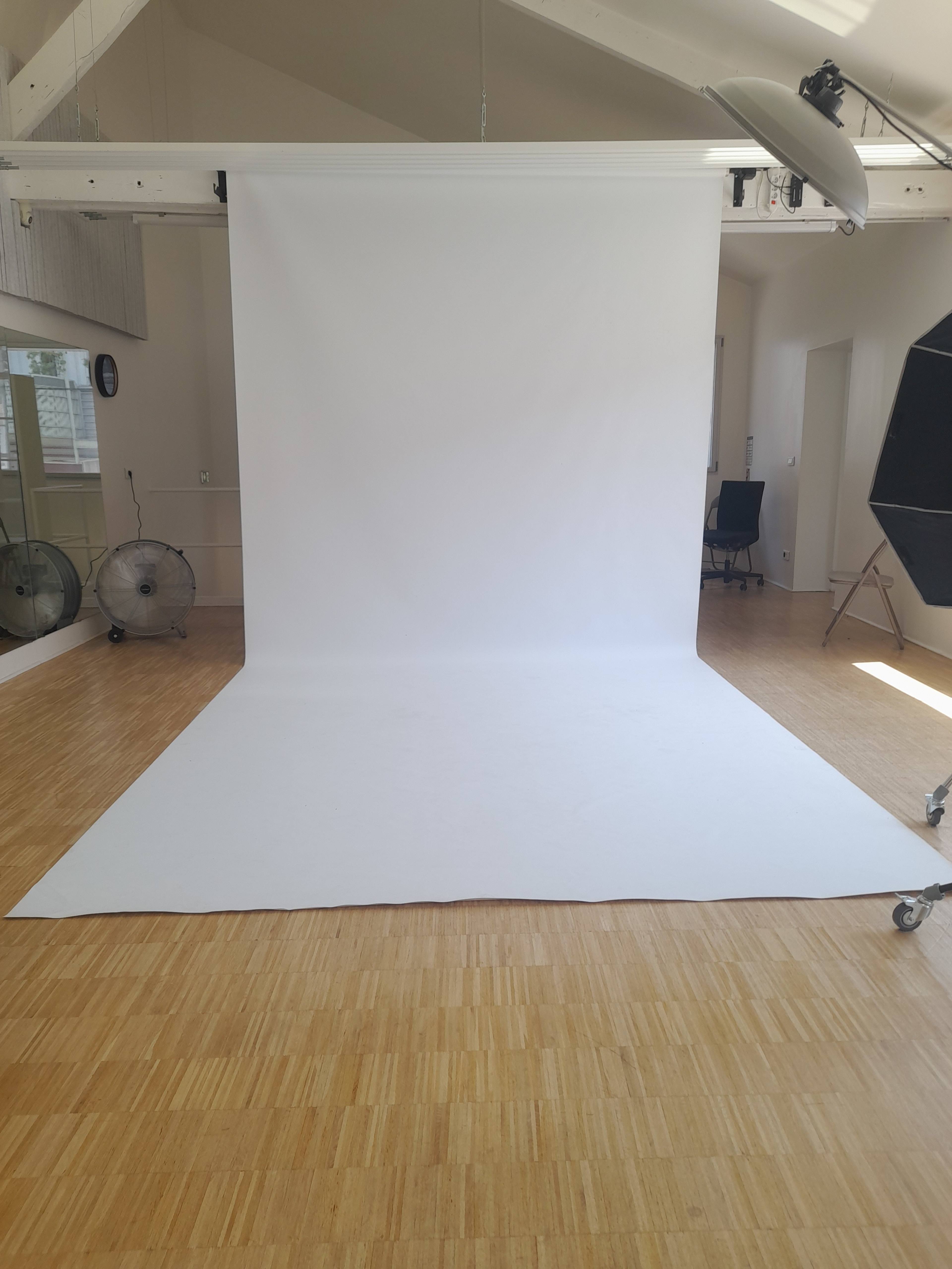 The image shows a spacious photo studio with a large white backdrop and wooden flooring.