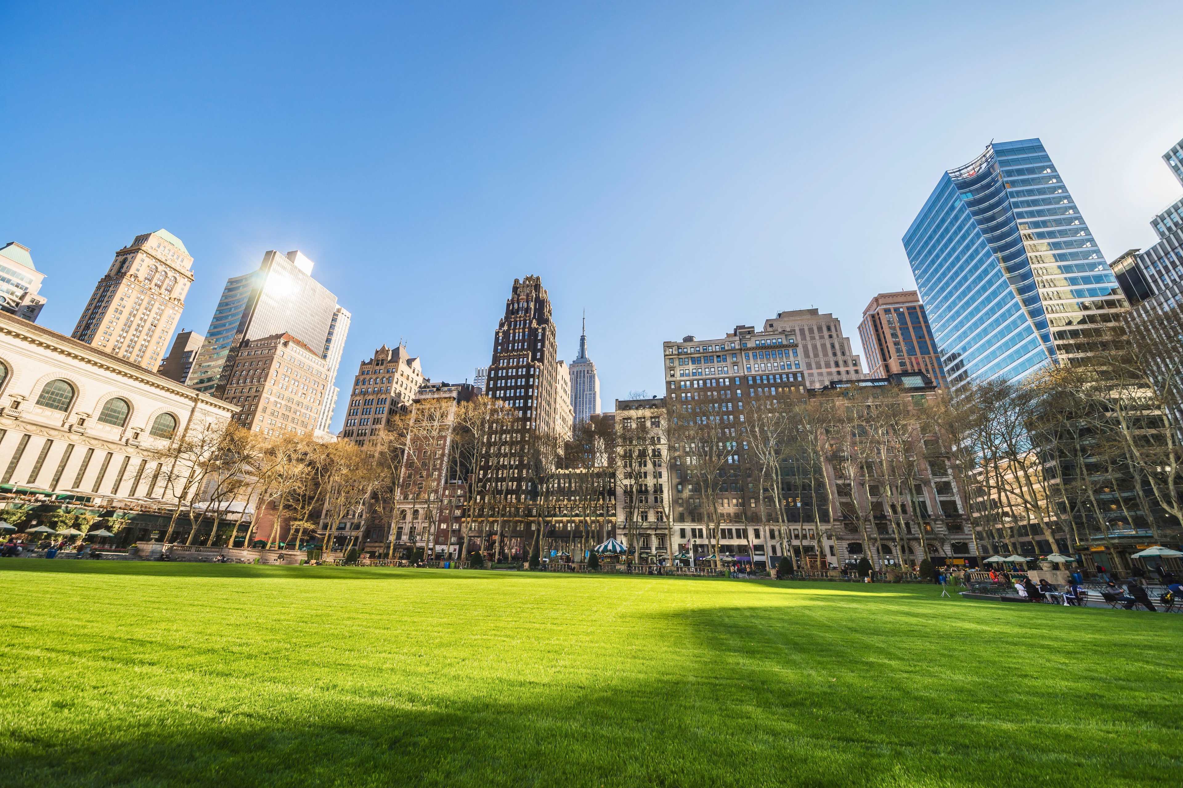 A wide expanse of green lawn is set against a backdrop of tall skyscrapers, including the Empire State Building, under a clear blue sky.