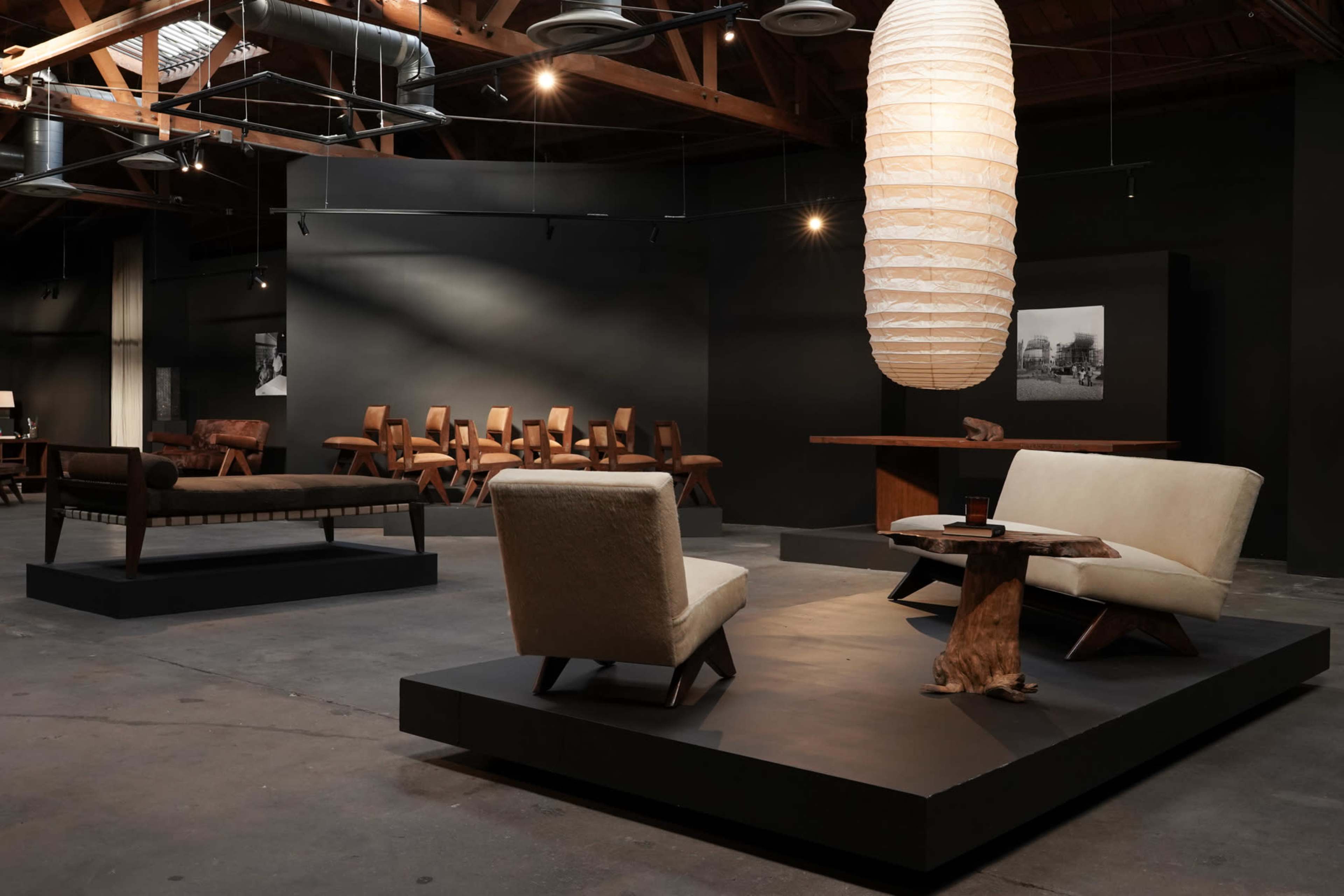The image shows a modern furniture showroom featuring four seating arrangements and a large hanging light fixture in a spacious, industrial setting.