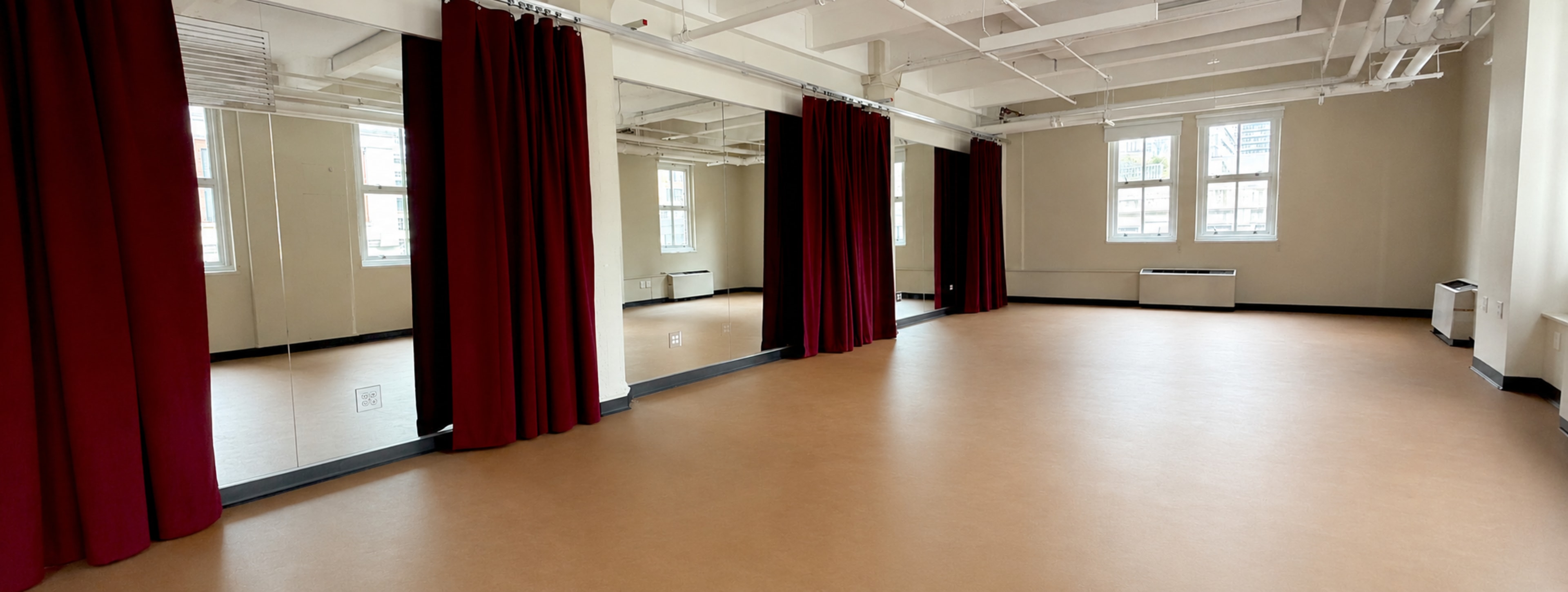 The image shows a spacious room with a smooth floor, large mirrors, and red curtains against white walls and large windows.