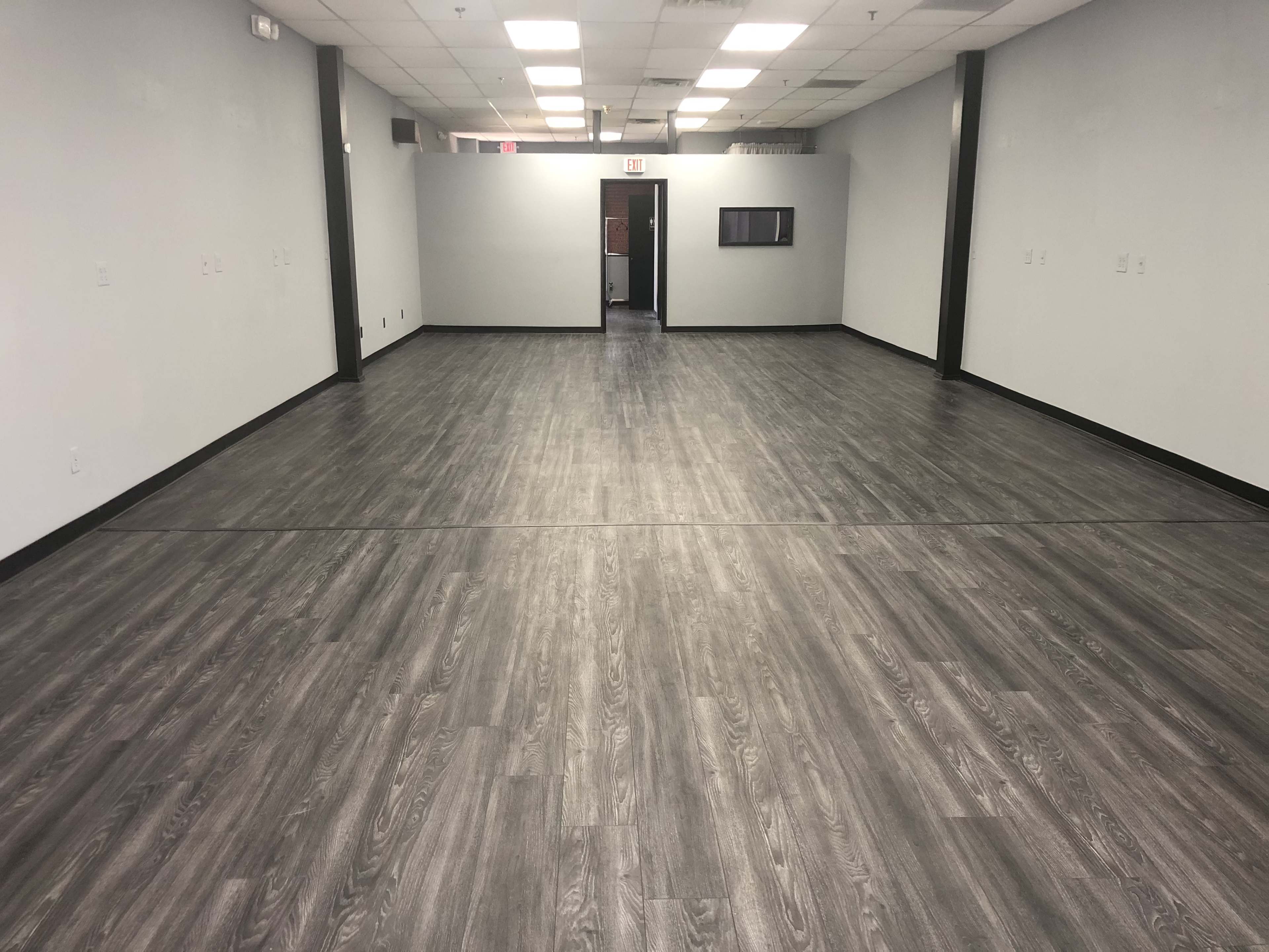 A spacious, empty room with gray laminate flooring and plain walls, featuring a doorway at the far end.