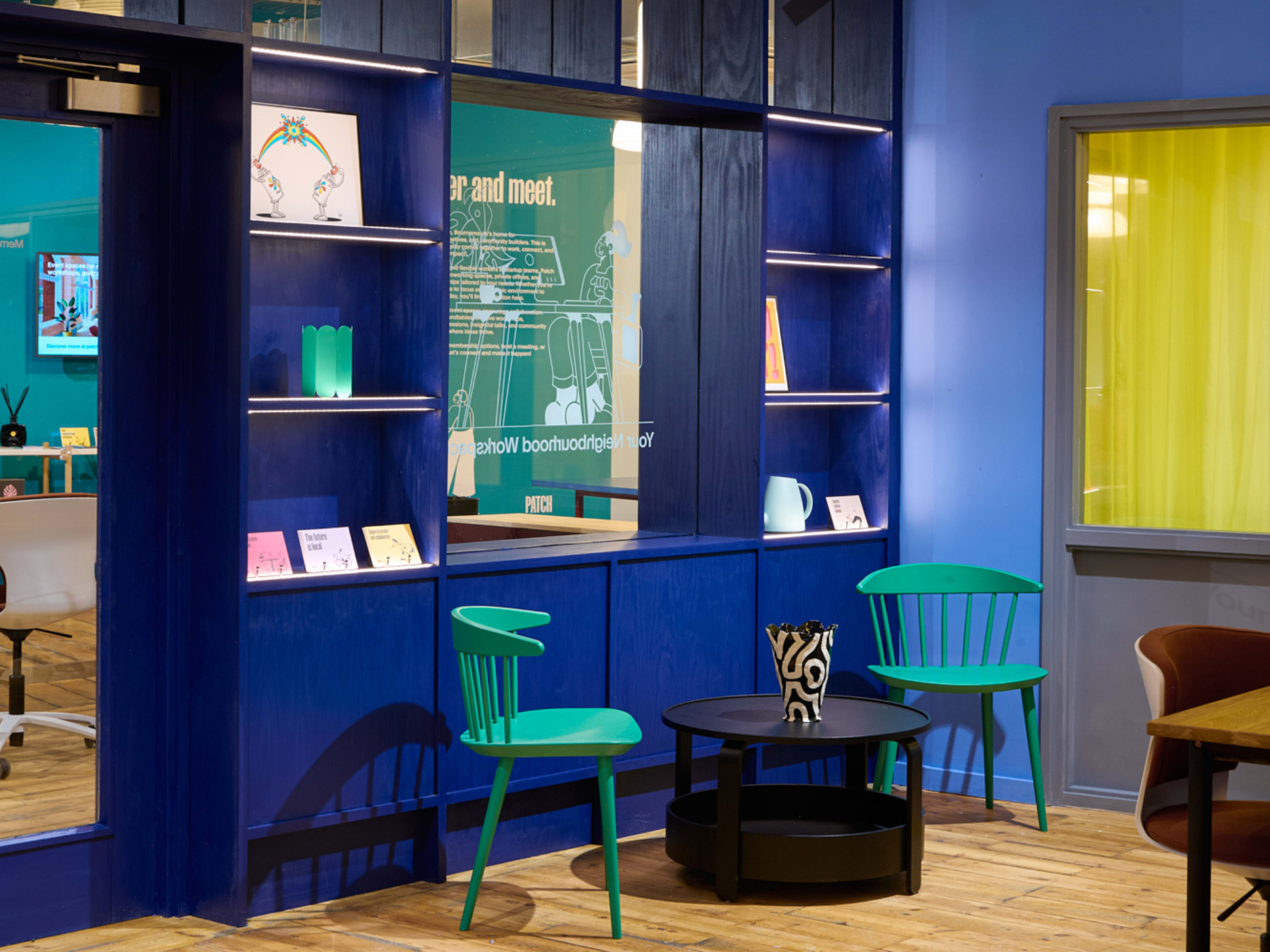 The image displays a modern interior scene featuring blue walls, wooden flooring, and a seating area with green chairs and a black coffee table.