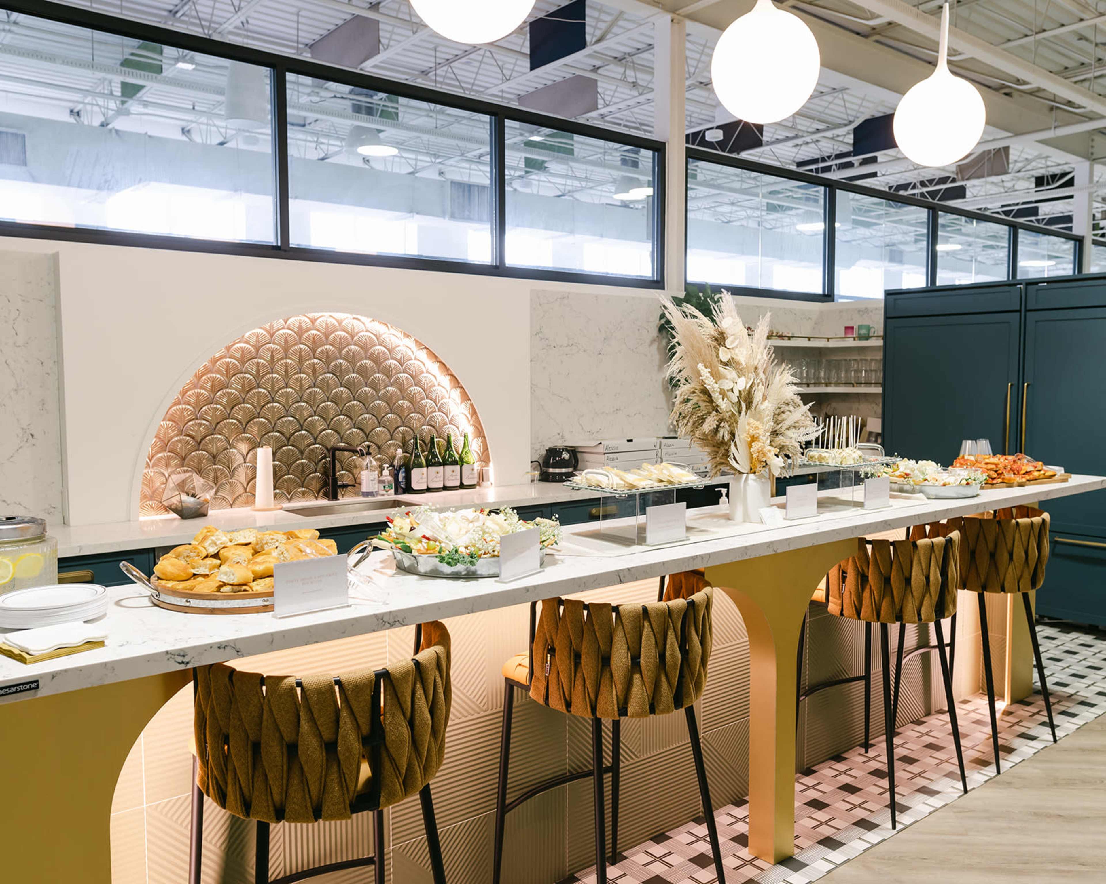 A modern buffet area features a marble counter adorned with various dishes, elegant lighting, and stylish bar stools.