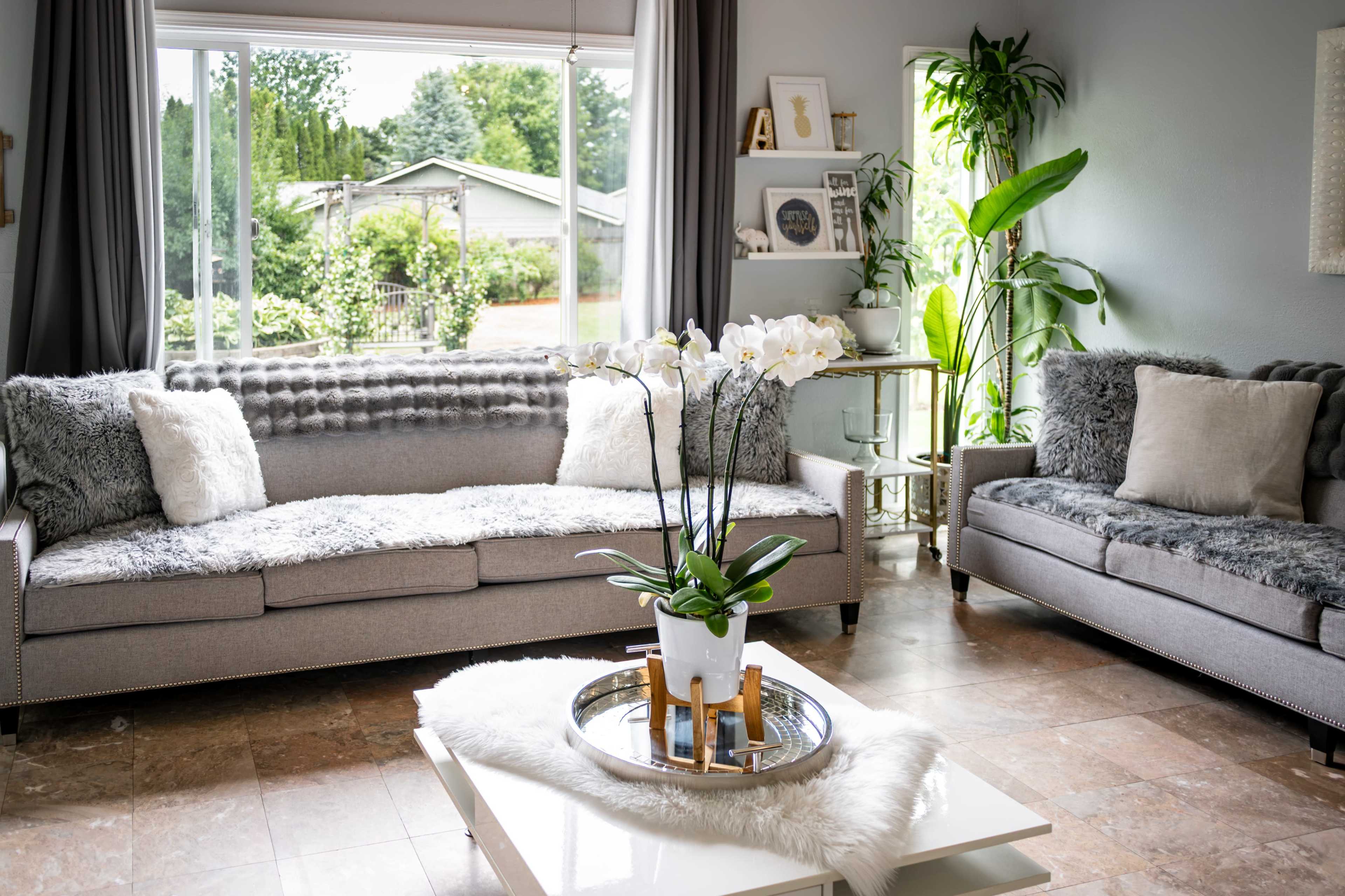 The living room features two sofas adorned with plush throws and a coffee table centered with a pot of white orchids.