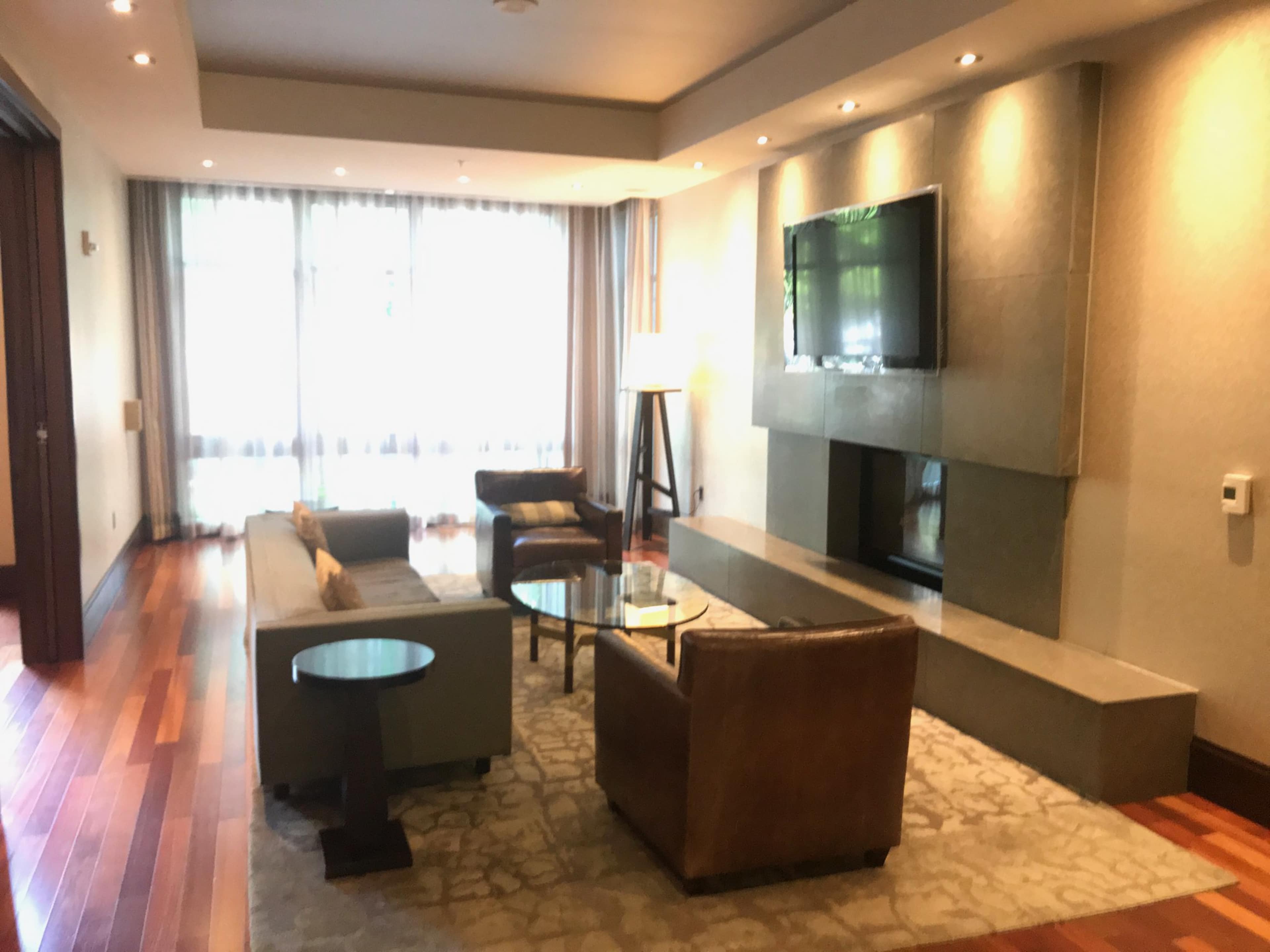 A modern living room features a television mounted on a stone wall, with seating arrangements consisting of two sofas, a coffee table, and wooden flooring.