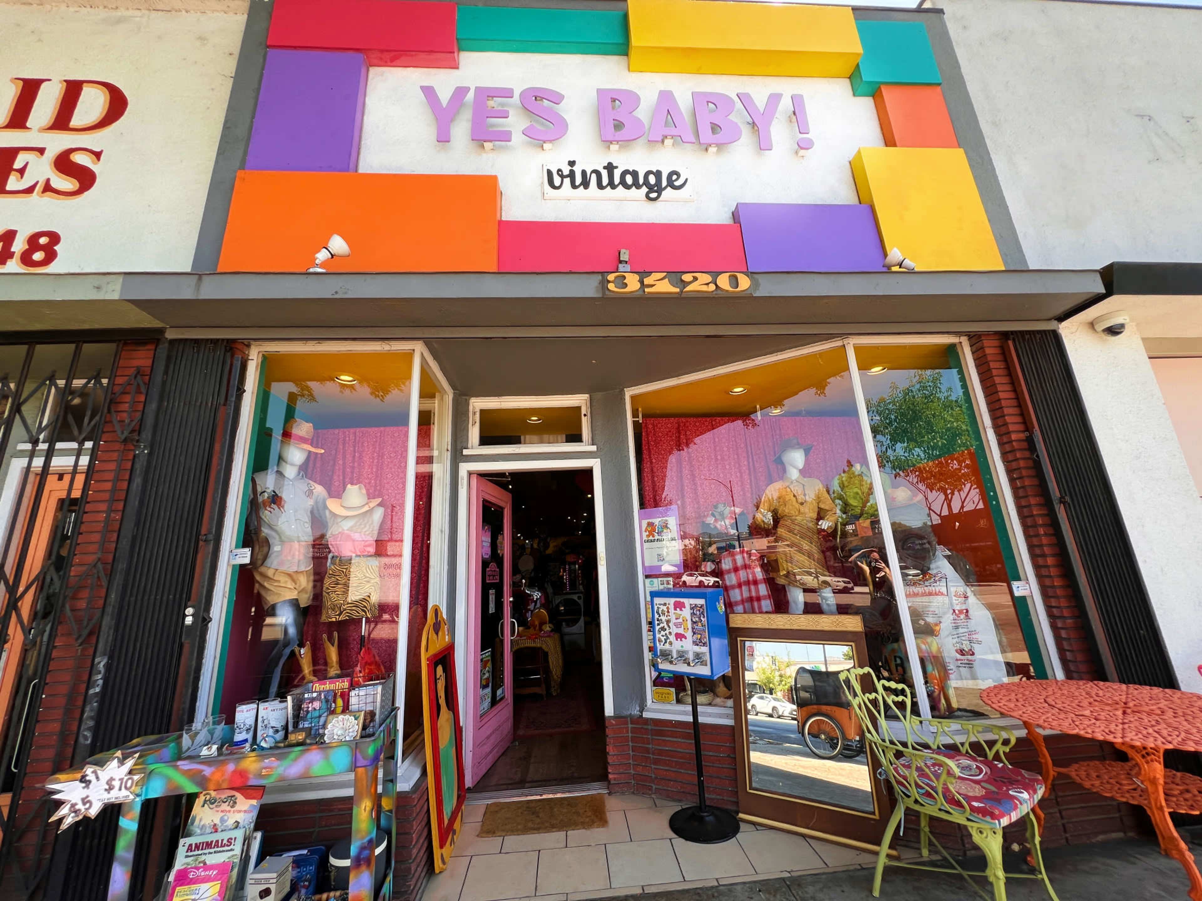 The storefront of a vintage shop named "YES BABY!" features colorful block signage and displays of clothing and accessories in the windows.