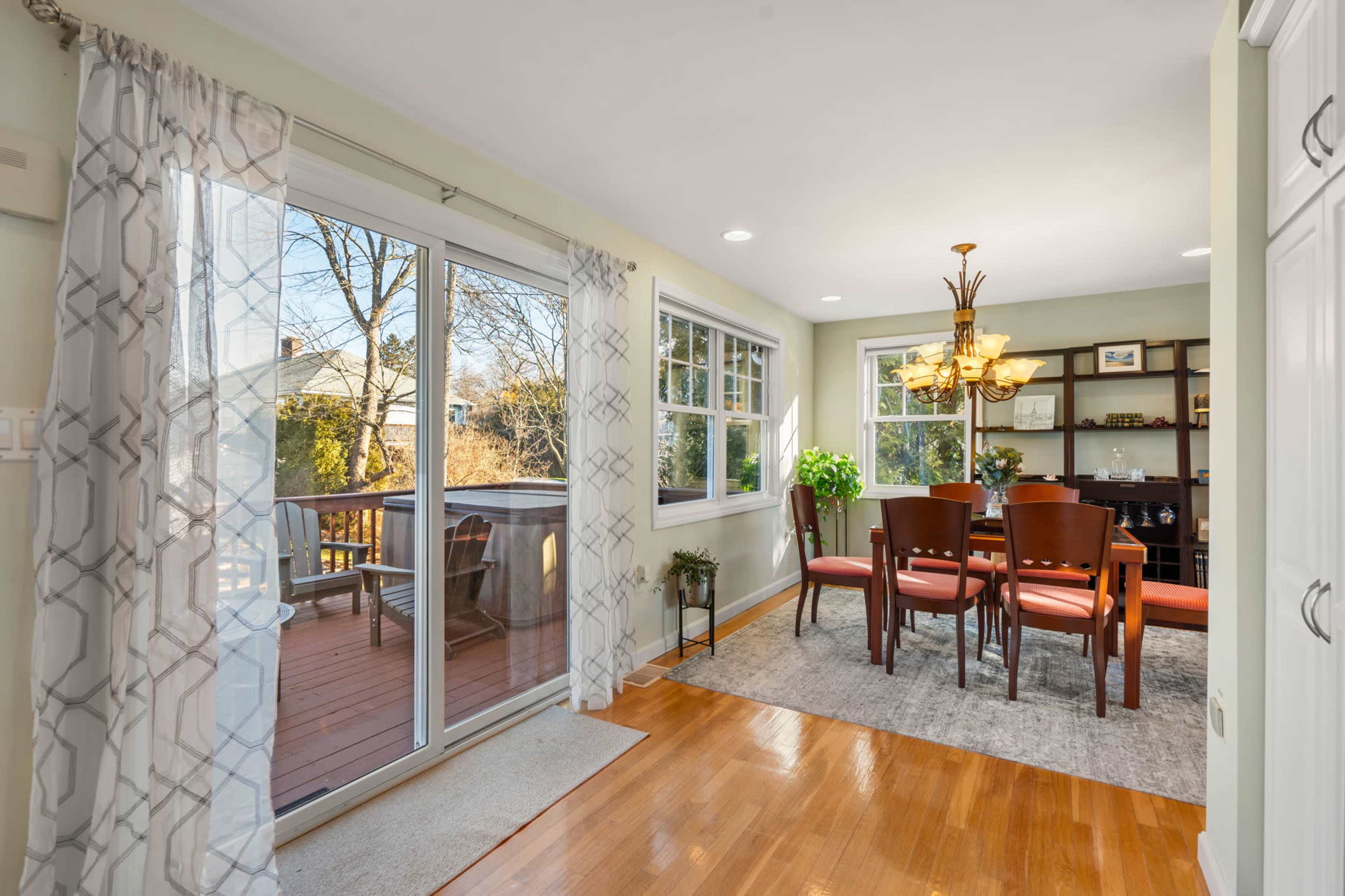 A bright dining area with a wooden table and chairs, adjacent to a glass door leading to an outdoor deck.
