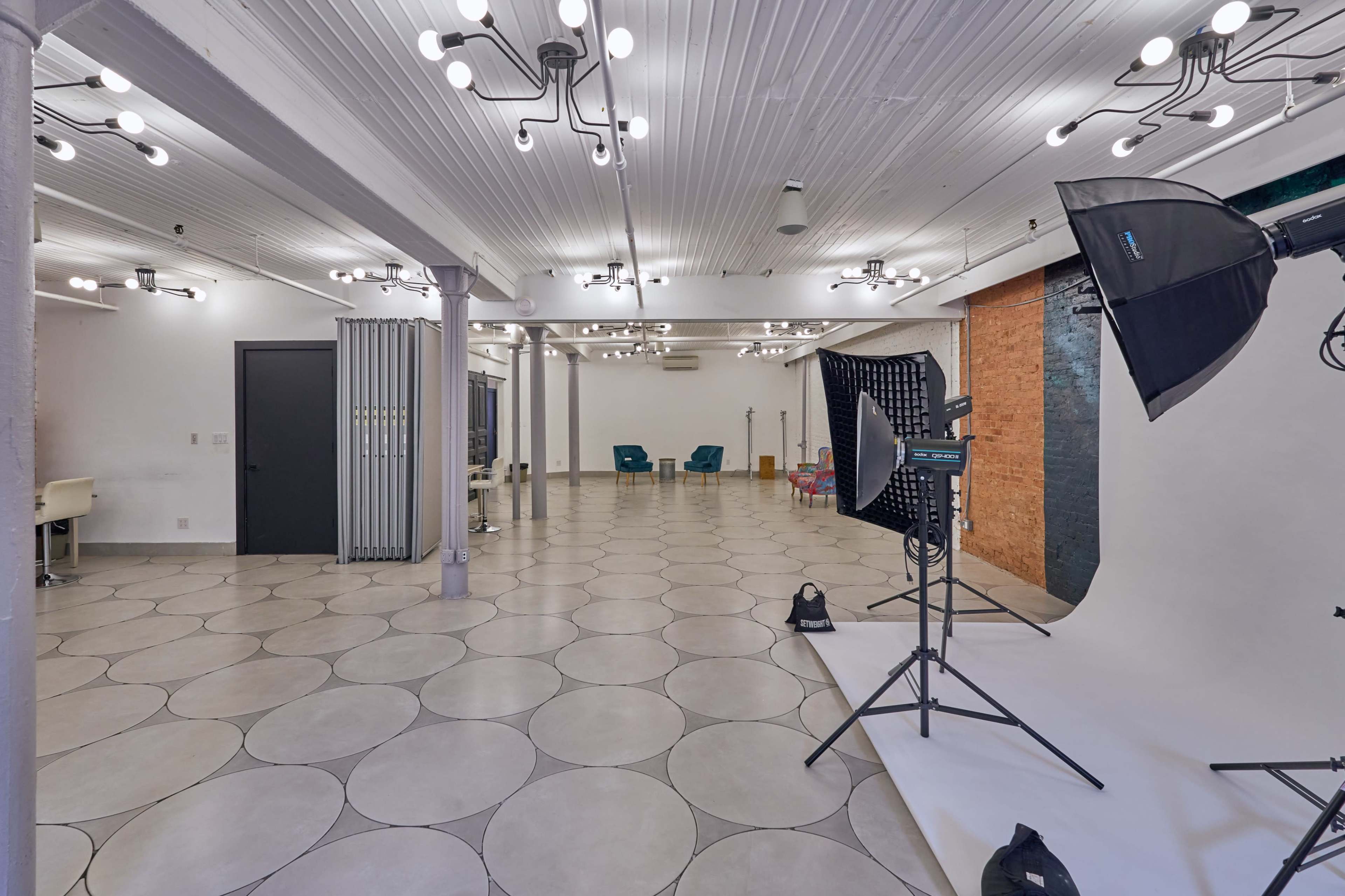 The image shows a spacious studio with a tiled floor, multiple ceiling lights, and photography equipment set up for a shoot.
