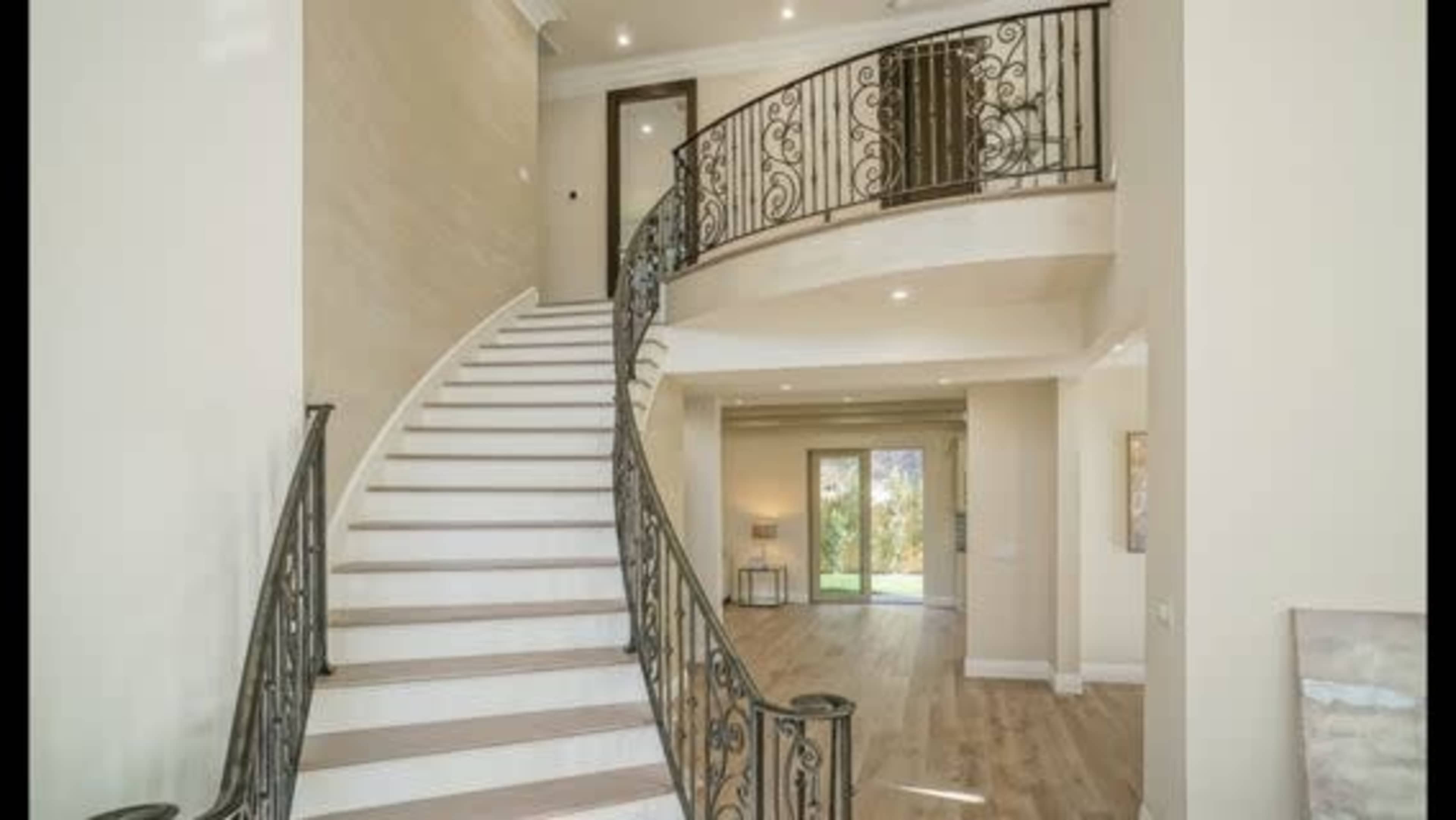 A curved staircase with wrought iron railing, leading to an upper level in an open, well-lit foyer.