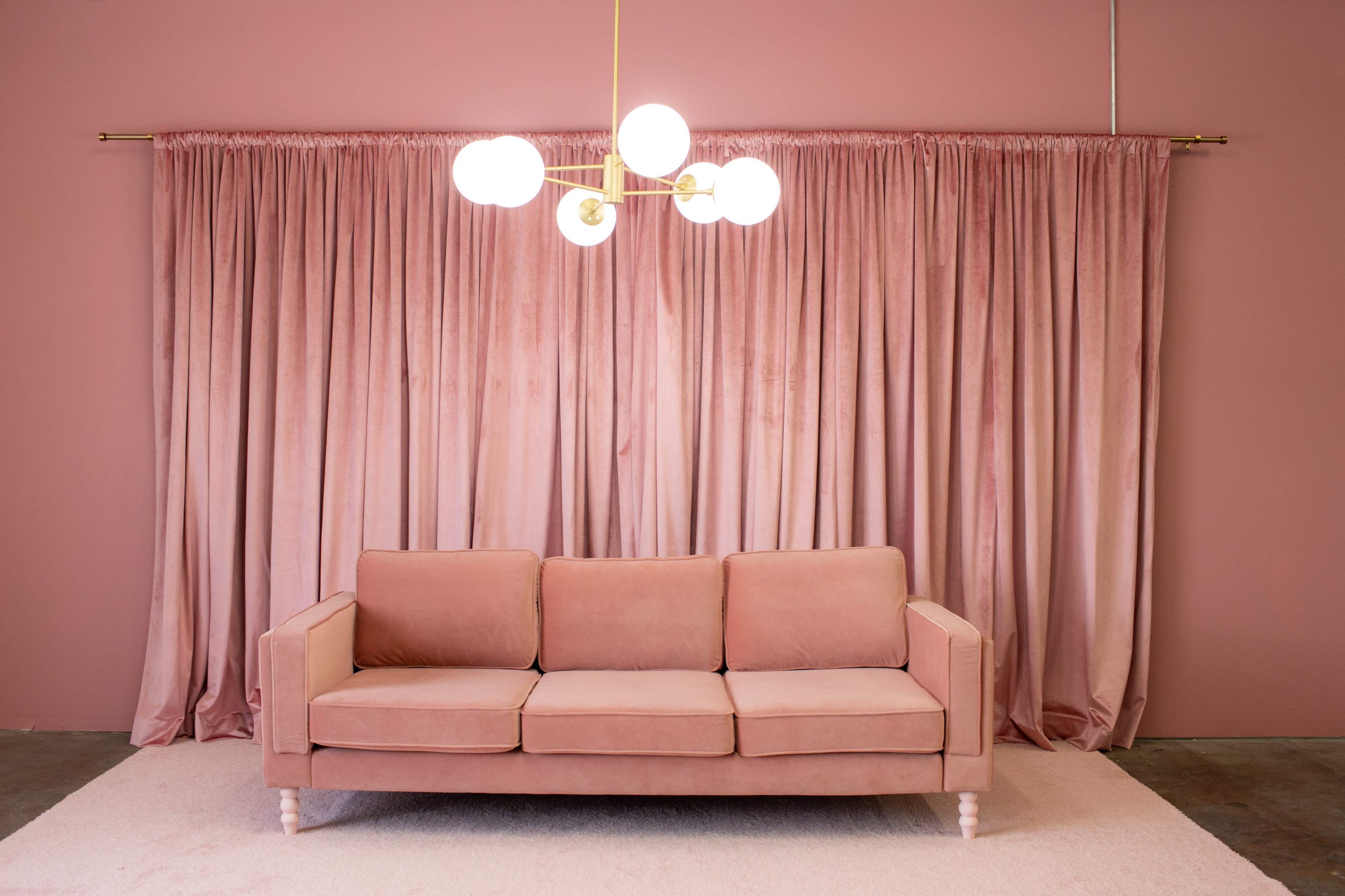 A pink sofa sits in front of a matching curtain, illuminated by a modern chandelier with spherical lights.
