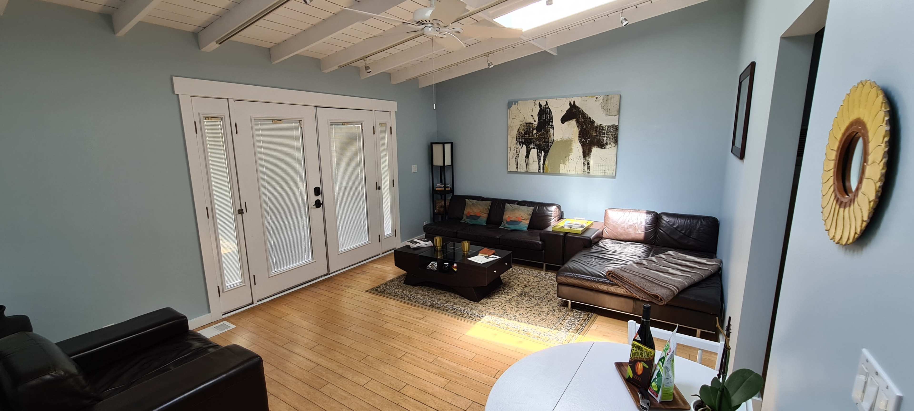 The image shows a well-lit living room with a black leather sectional sofa, a coffee table, and sliding glass doors leading to an outdoor area.