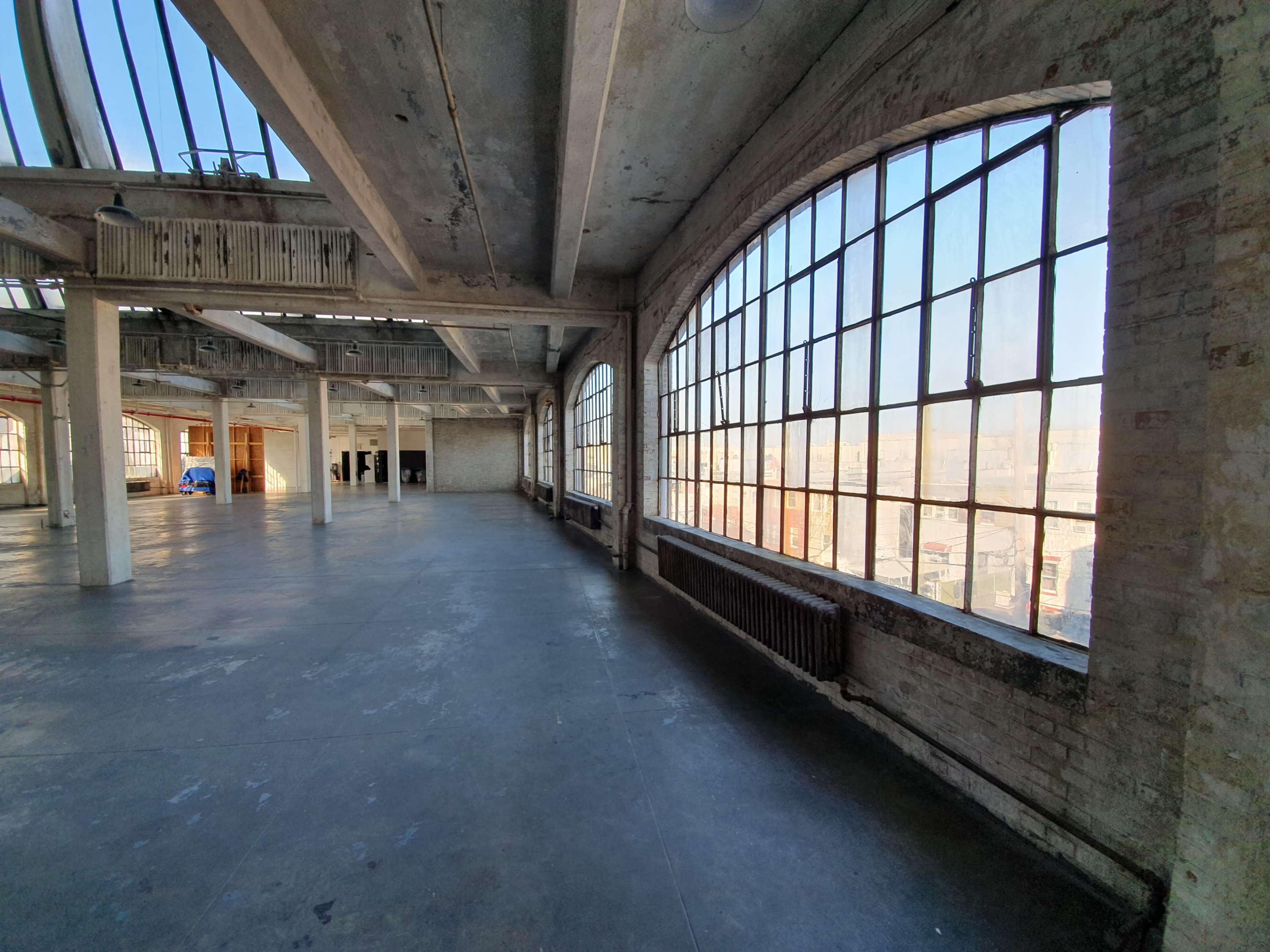 An empty industrial space with large arched windows, exposed brick walls, and concrete ceilings.