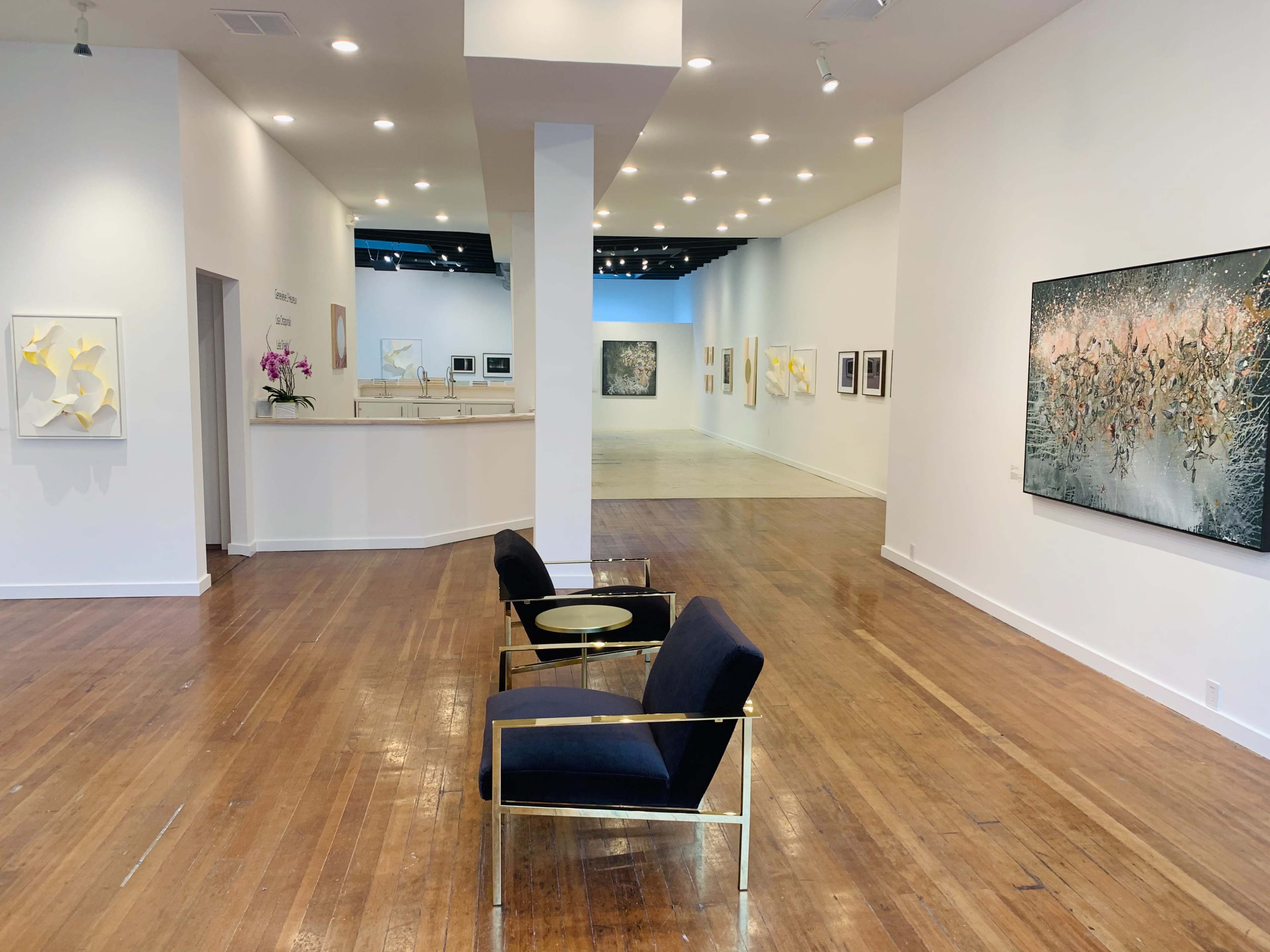 A modern gallery space with a reception area,white walls adorned with framed artwork, and a seating area featuring contemporary chairs.