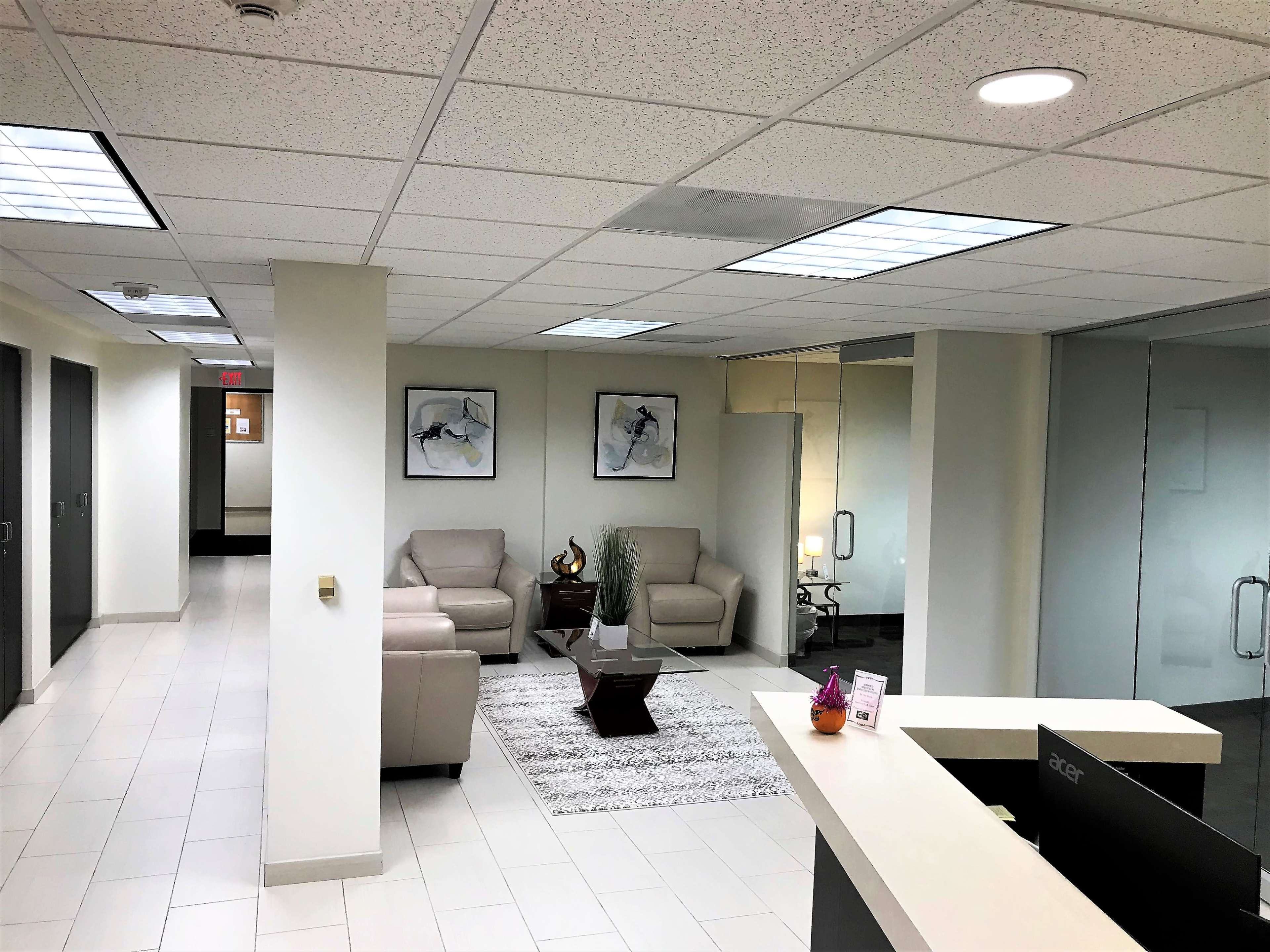 A modern office reception area featuring a seating arrangement with two armchairs, a decorative table, and artwork on the walls.