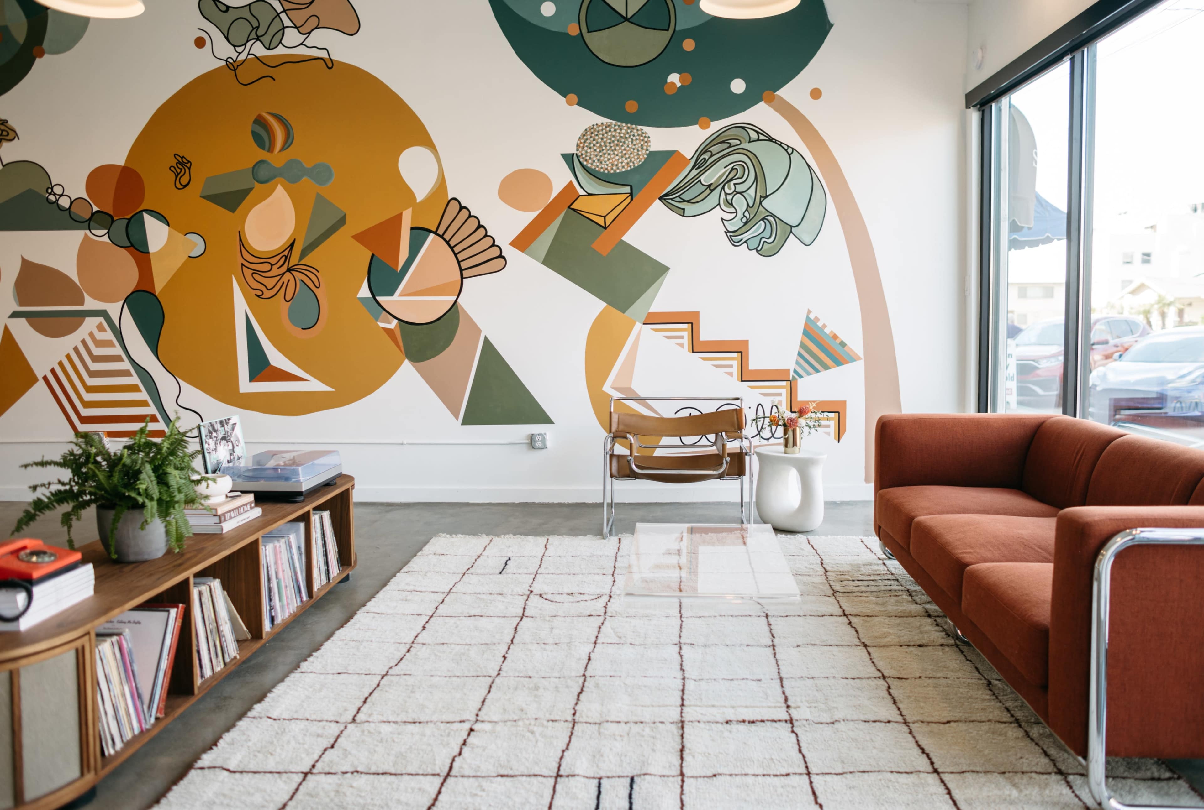 The image shows a modern interior with a patterned wall mural, a brown couch, a coffee table, and a rug on a concrete floor.