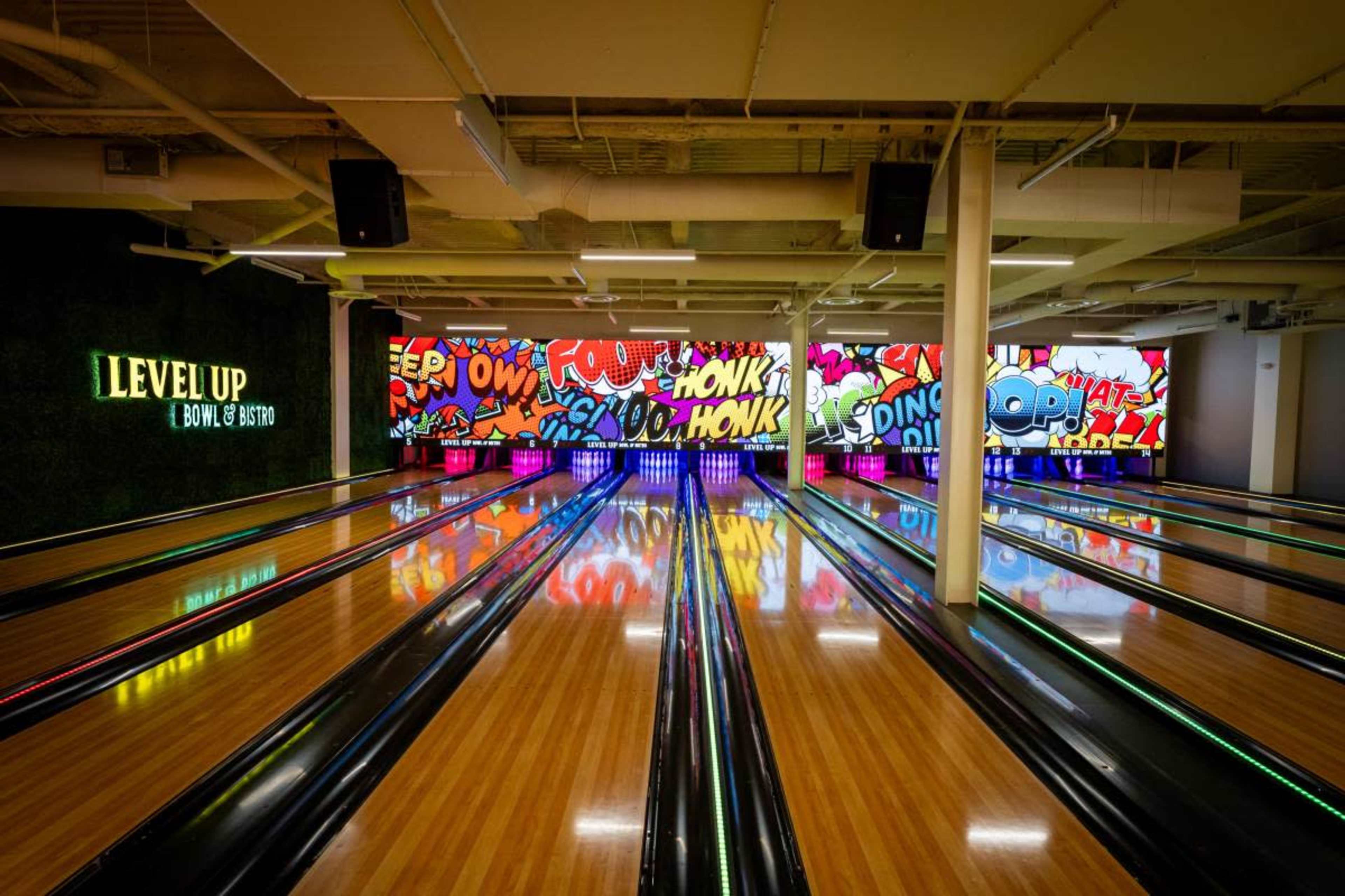 The image shows a bowling alley with brightly lit lanes and a colorful graffiti-style mural on the back wall.