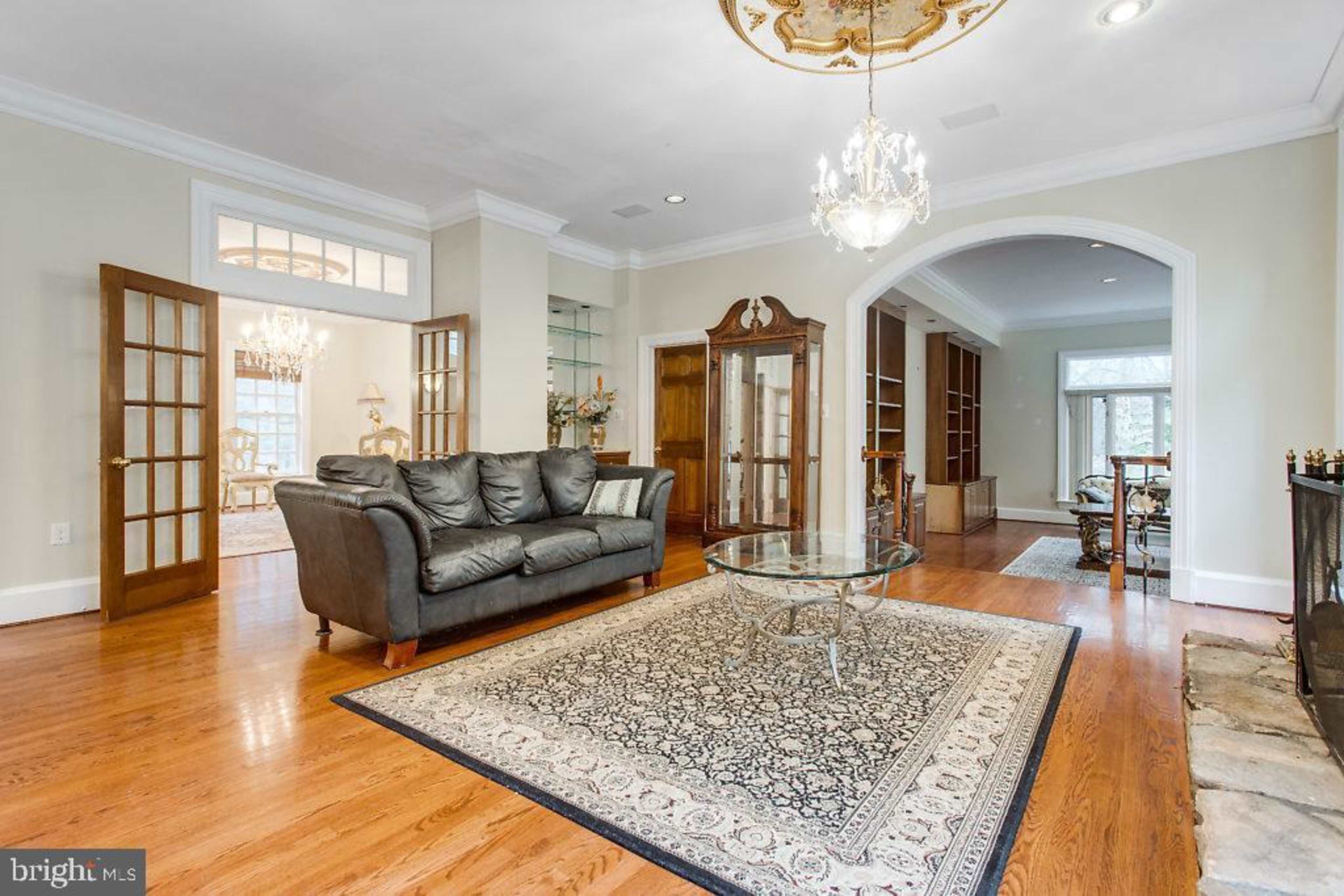 A spacious living room with hardwood floors, a glass coffee table, and a leather sofa, leading to an arched doorway that opens into another room.