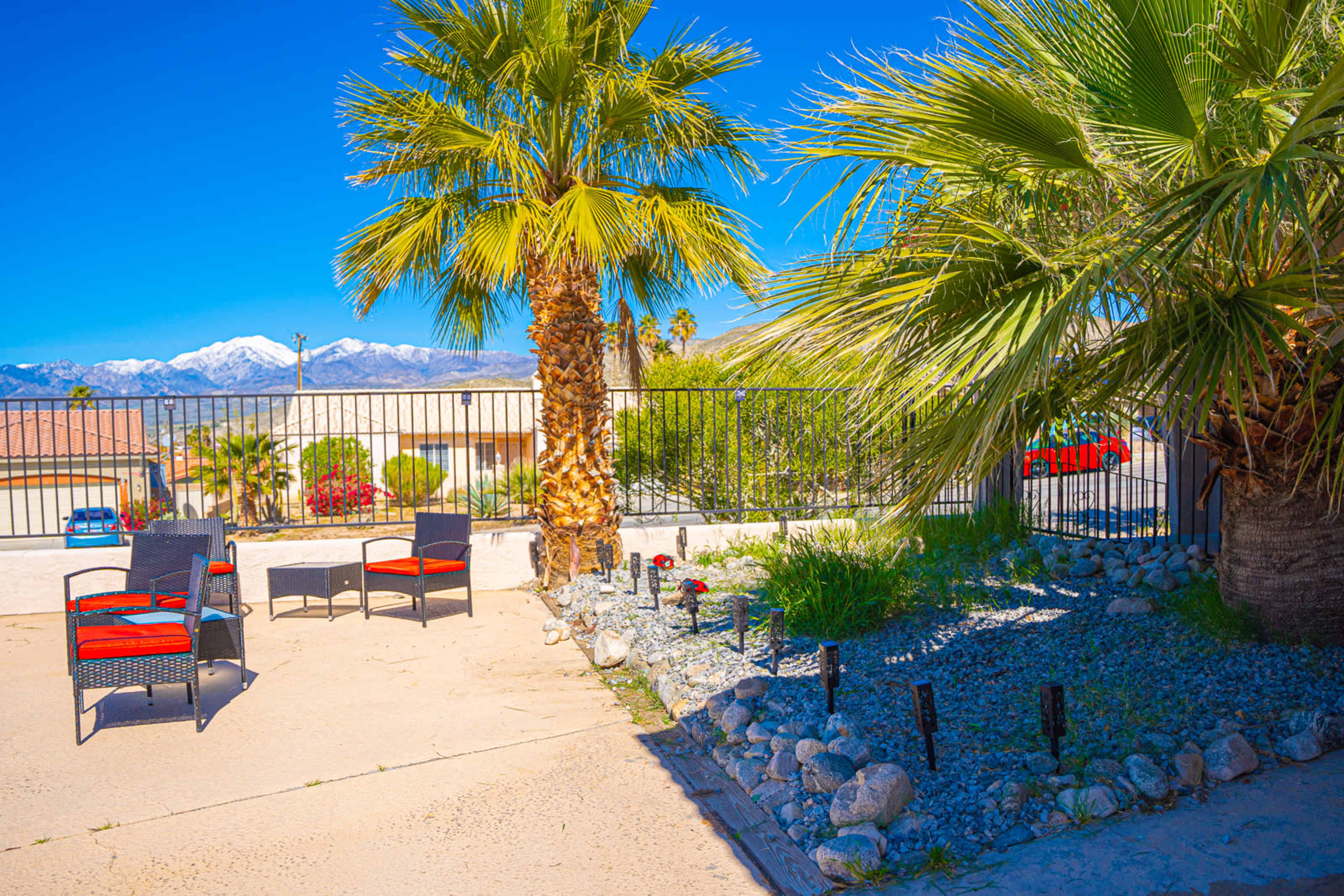 A seating area with chairs arranged around a palm tree and a gravel garden, set against a backdrop of mountains.