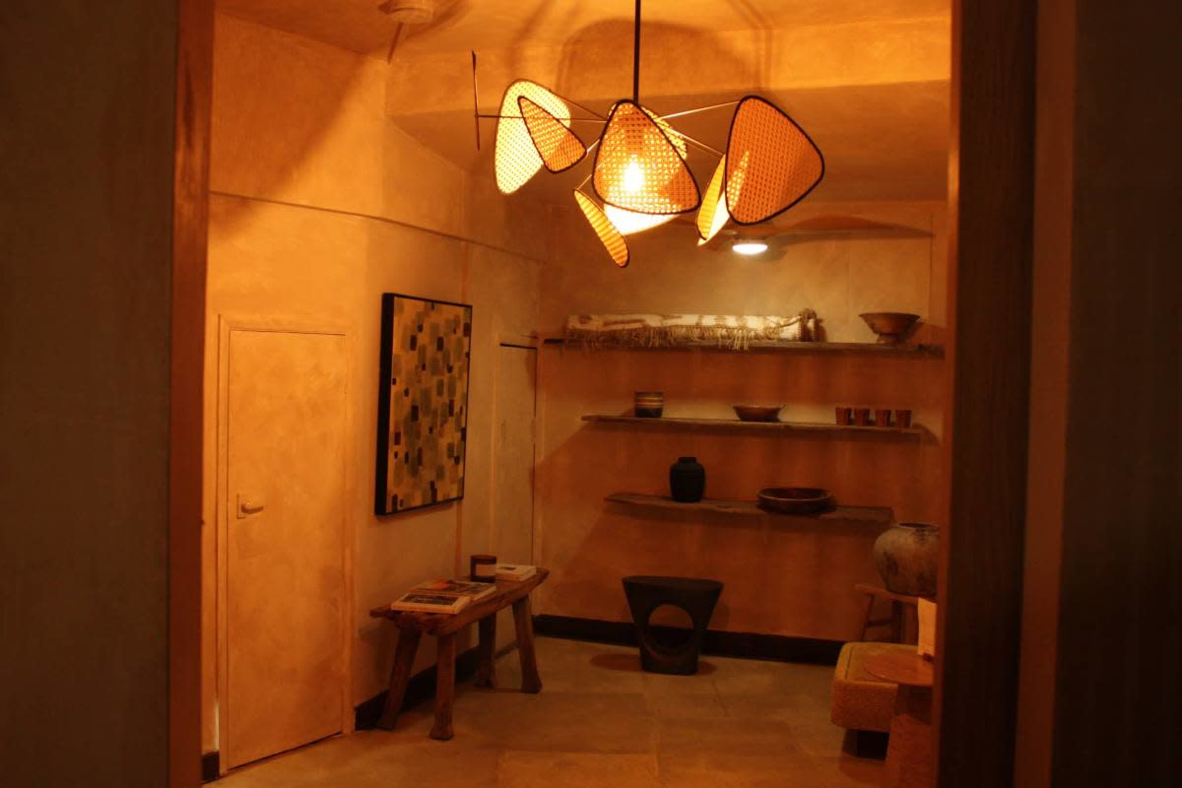 A warmly lit interior space featuring a modern light fixture, shelves with decor items, a wooden table, and a door.